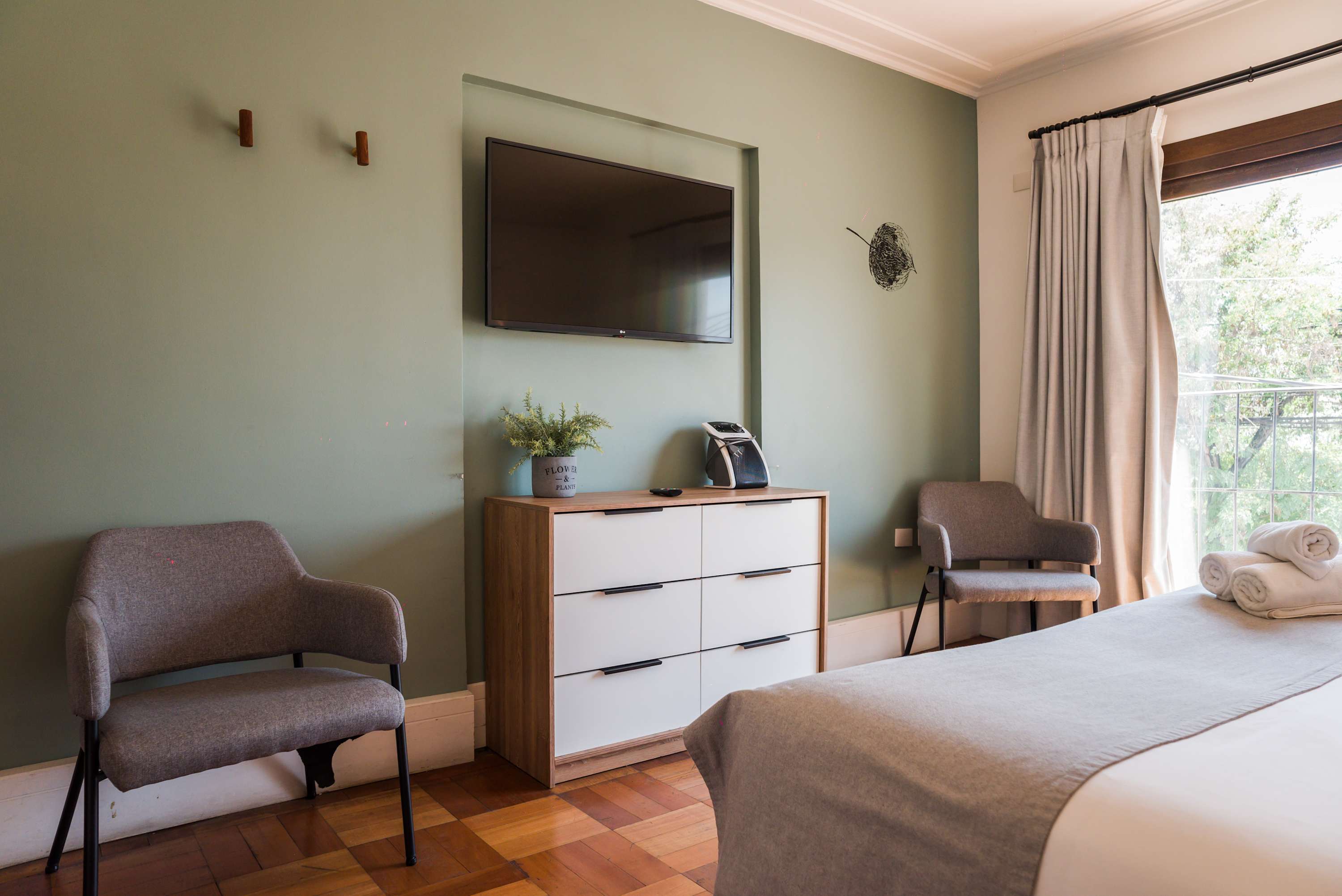 Cozy bedroom with a serene green accent wall, comfy seating, and natural light. Perfect for relaxation after exploring the city.