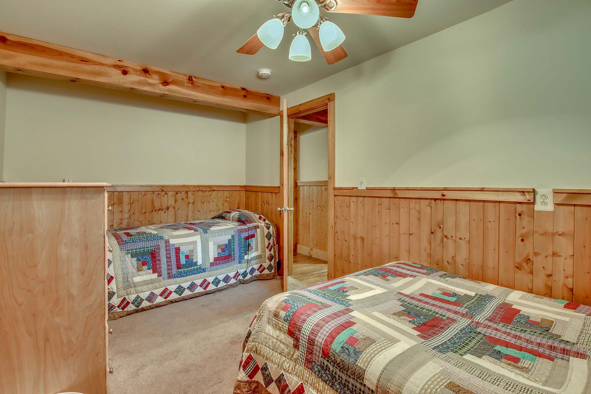 Twin beds with charming quilts beneath a vaulted ceiling with ceiling fan