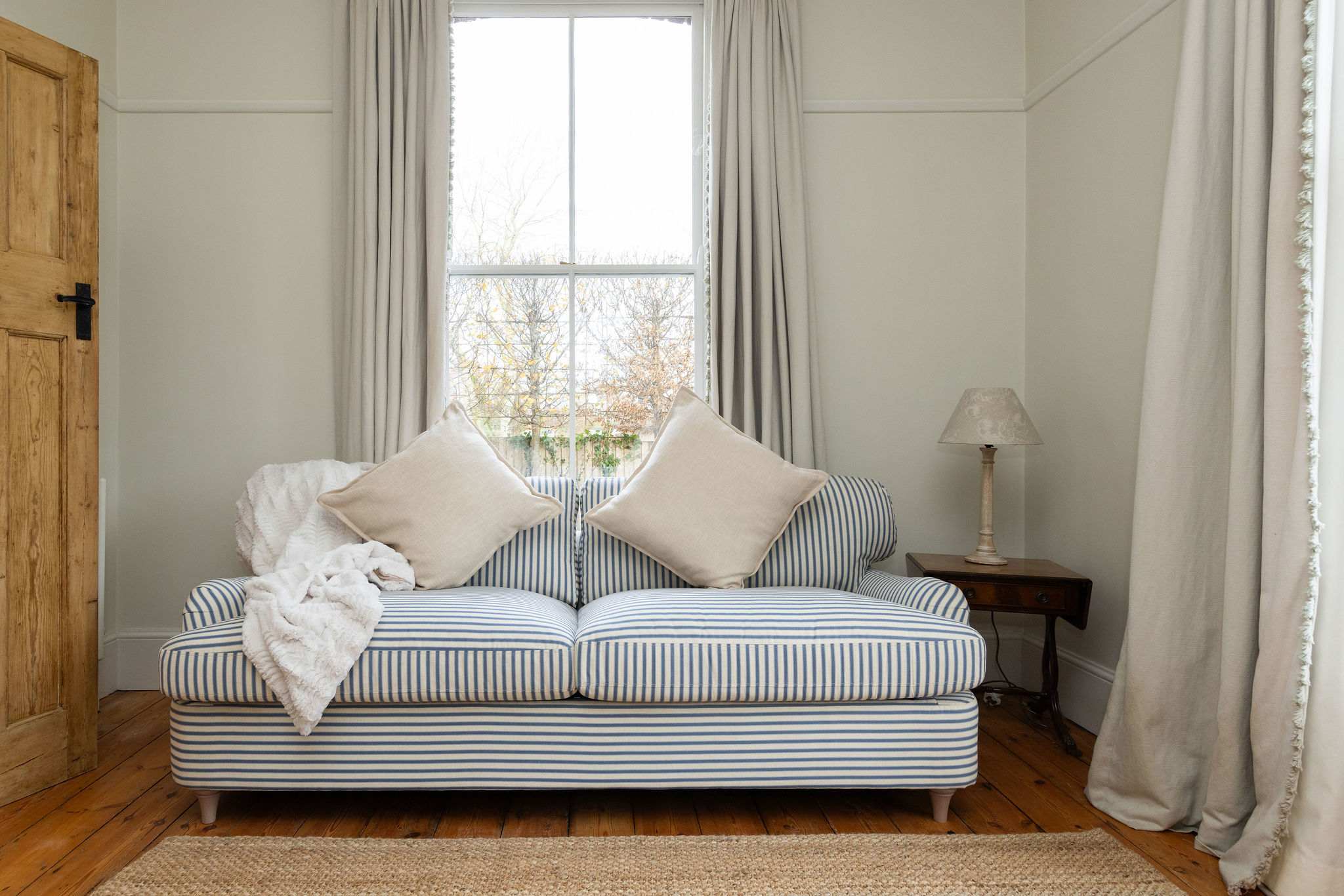 Cosy striped sofa bed beneath tall sash windows