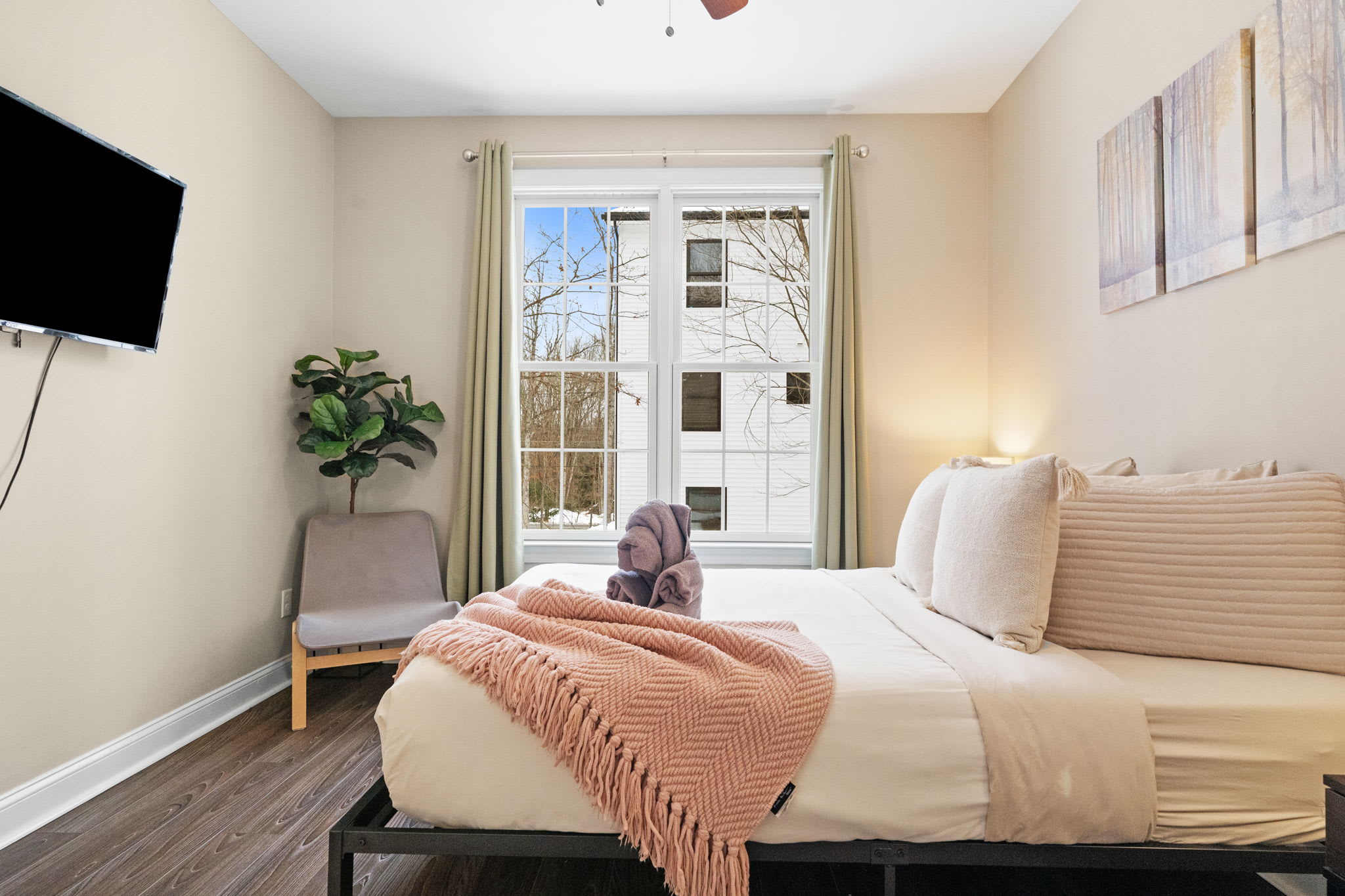 Charming guest bedroom featuring queen bed, warm wood floors and bright natural lighting
