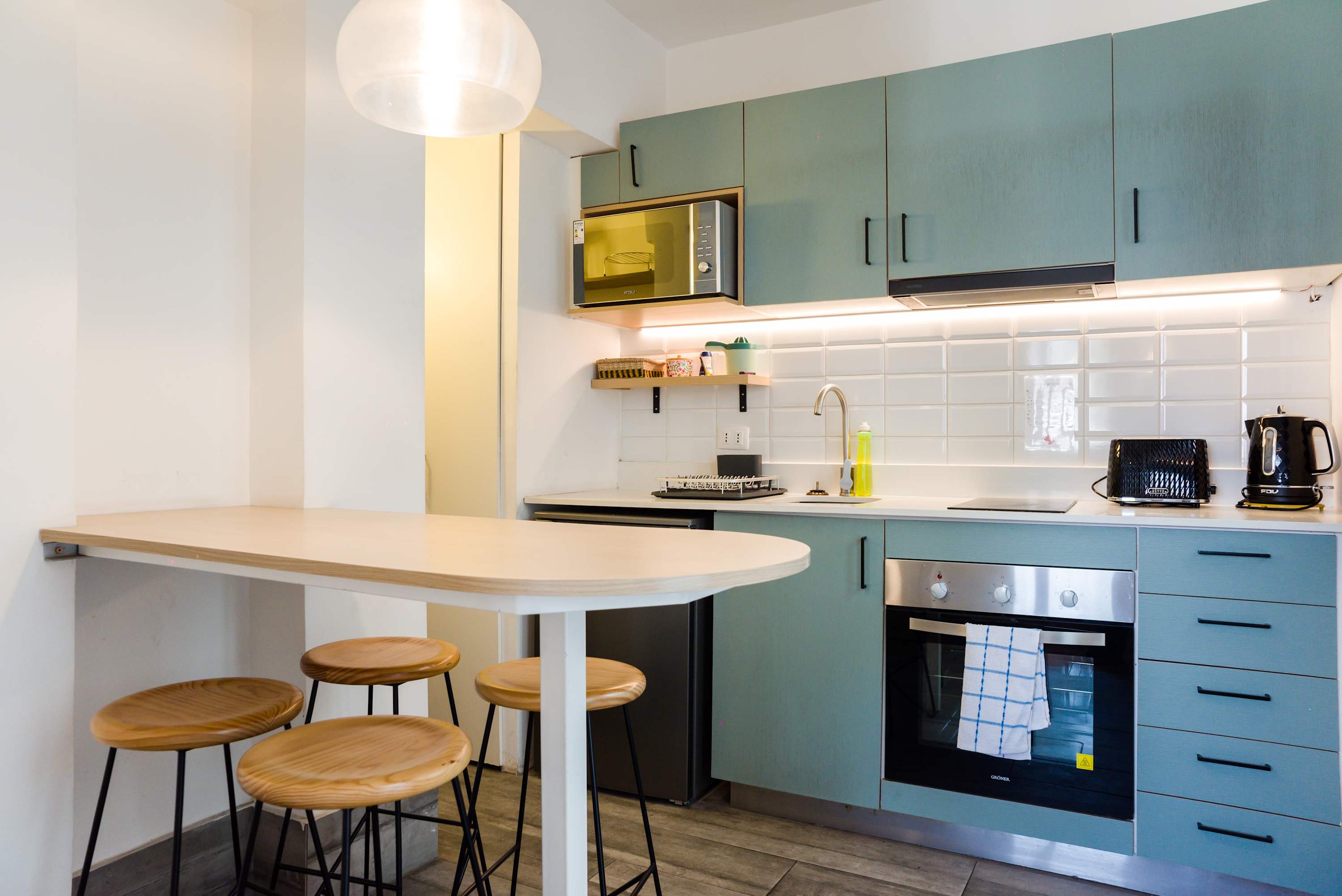 Modern kitchen with sleek teal cabinets and a cozy breakfast bar, perfect for enjoying meals in this stylish studio.