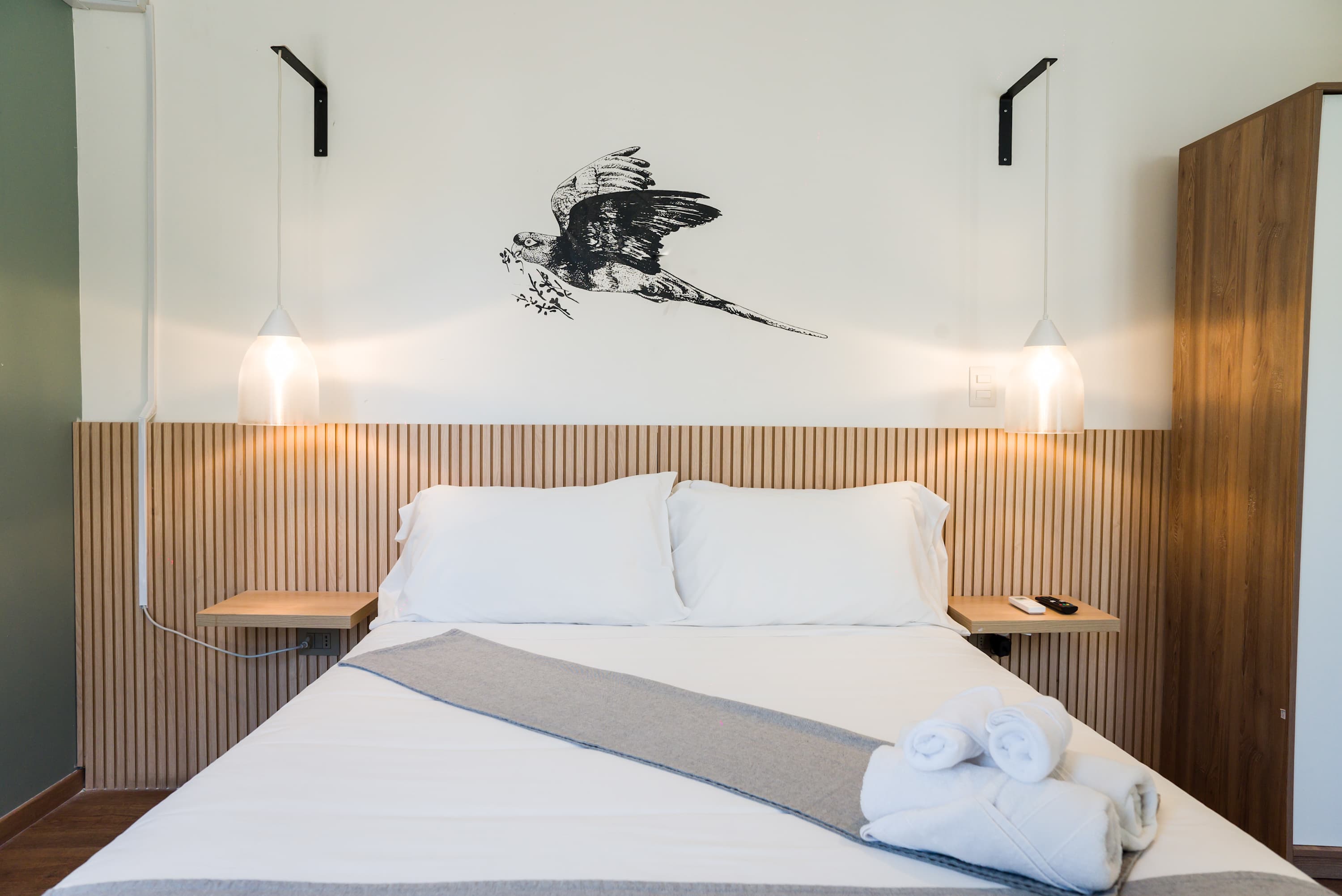 Cozy bedroom with stylish pendant lighting and a unique bird mural, perfect for a restful stay.