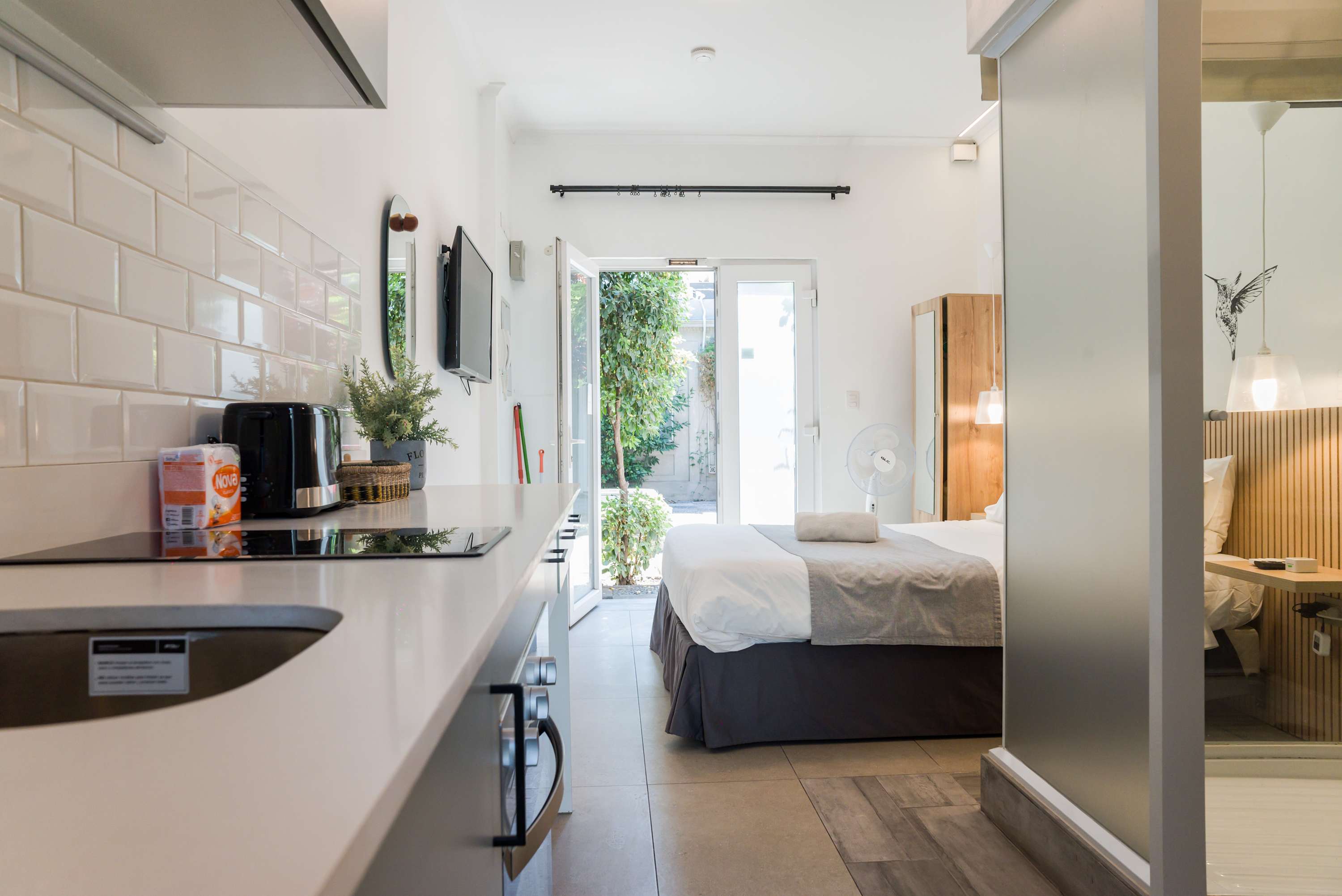 Chic studio with modern kitchen and cozy sleeping area, opening to a serene outdoor view.