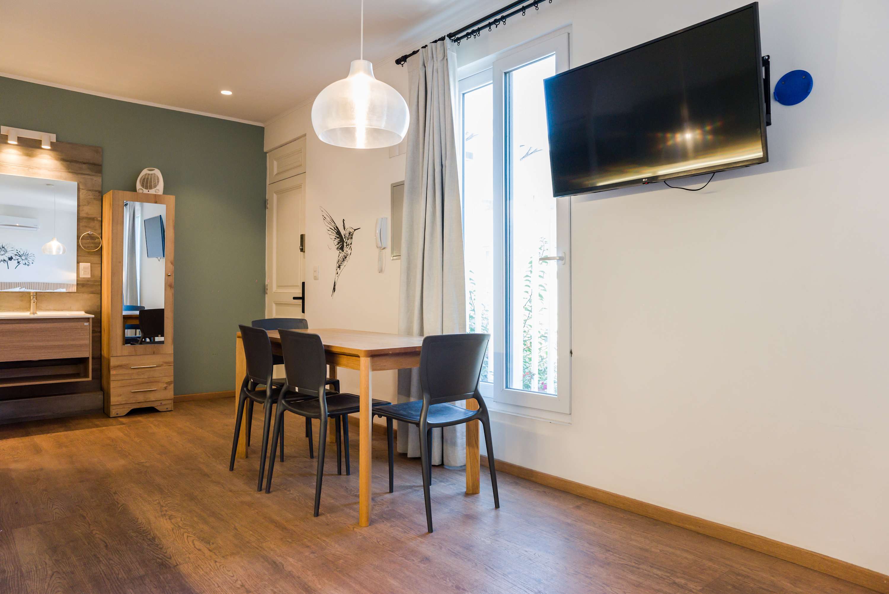 Bright and modern dining area with a wall-mounted TV and ample natural light, perfect for cozy meals.