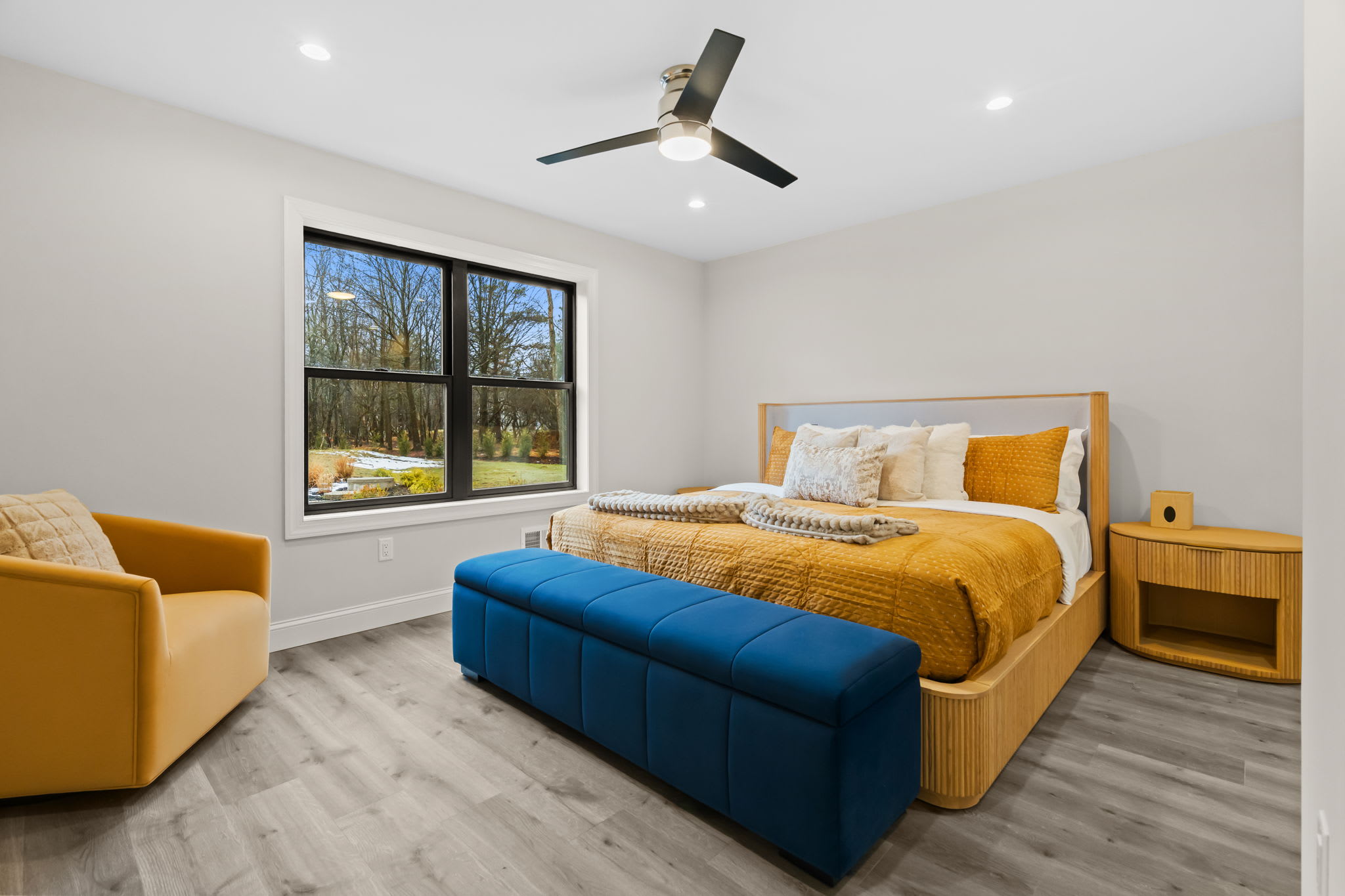 Spacious bedroom with golden bedding and teal velvet bench overlooking the forest