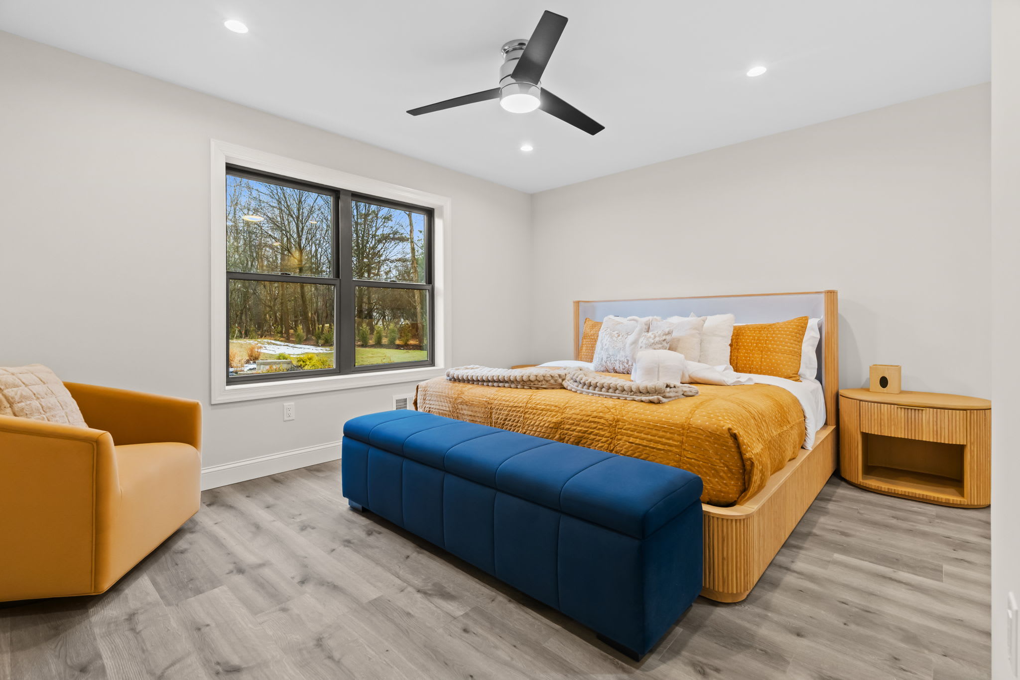 The bedroom offers a storage bench and ceiling fan with views of the forest beyond