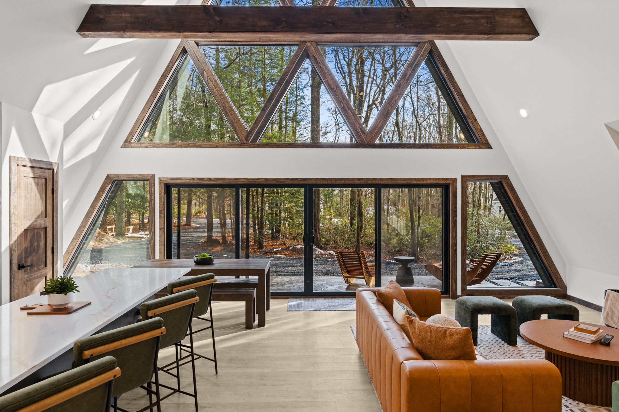 Sunlit living room with soaring A-frame windows framing endless forest views