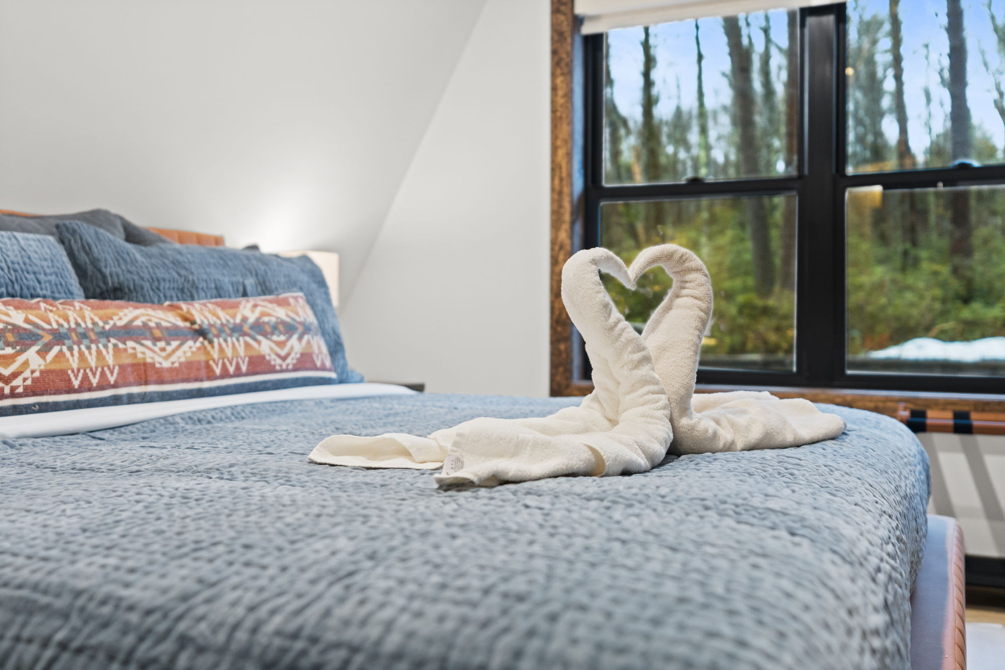 A welcoming towel swan greets you on the king bed with forest views beyond