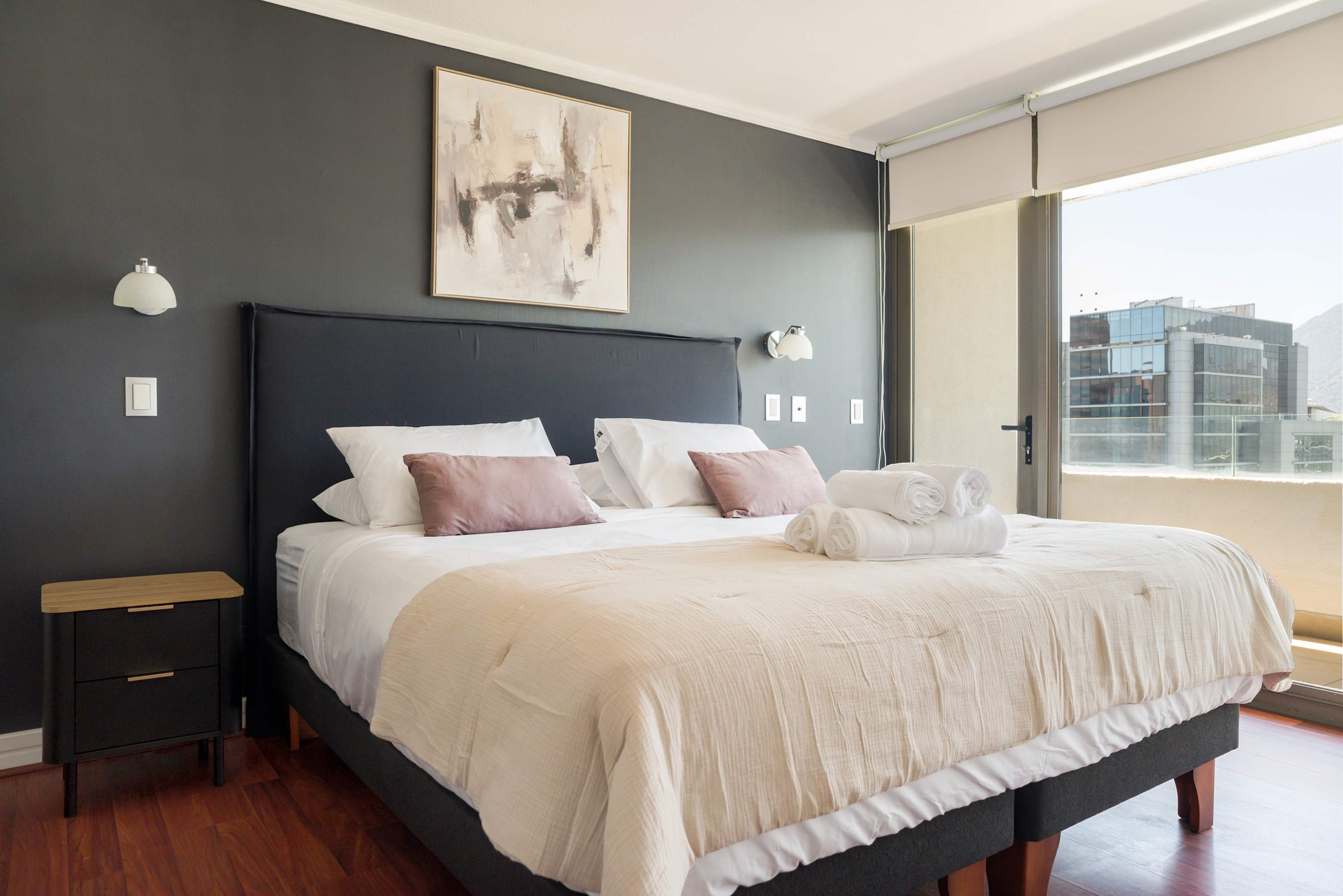 Relax in this stylish bedroom with a city view, featuring cozy bedding and modern decor.