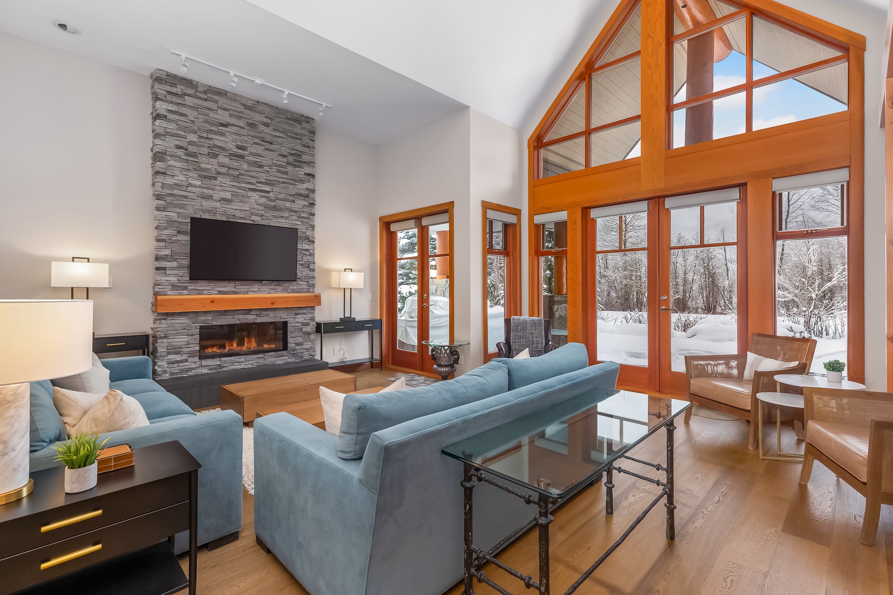 - Inviting living room featuring stone fireplace and cozy blue seating 
- Floor-to-ceiling windows flood the space with natural light and scenery 
- A perfect blend of comfort and elegance for relaxing evenings indoors 