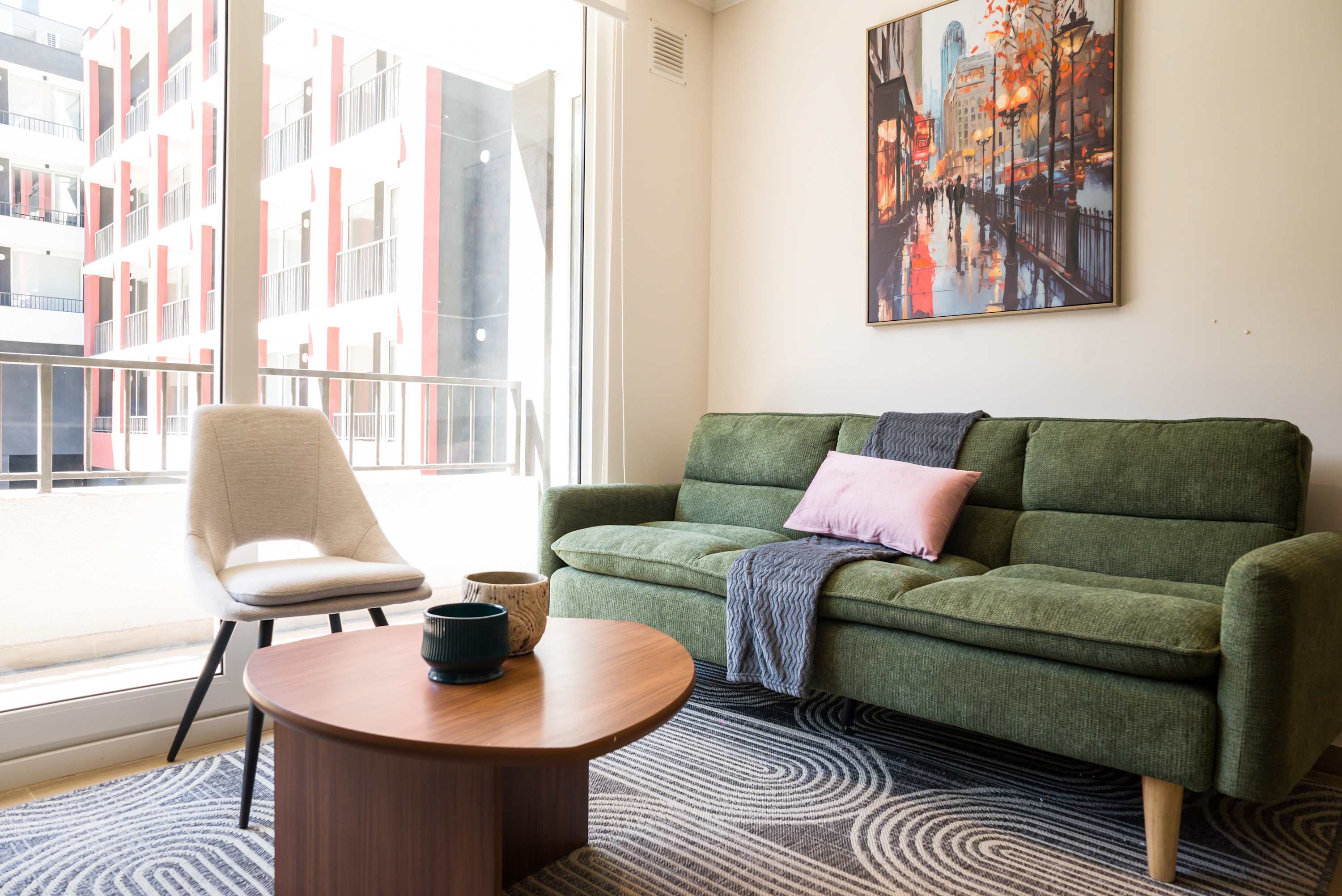 Relax in this bright and cozy living room with a stylish green sofa and vibrant cityscape art.