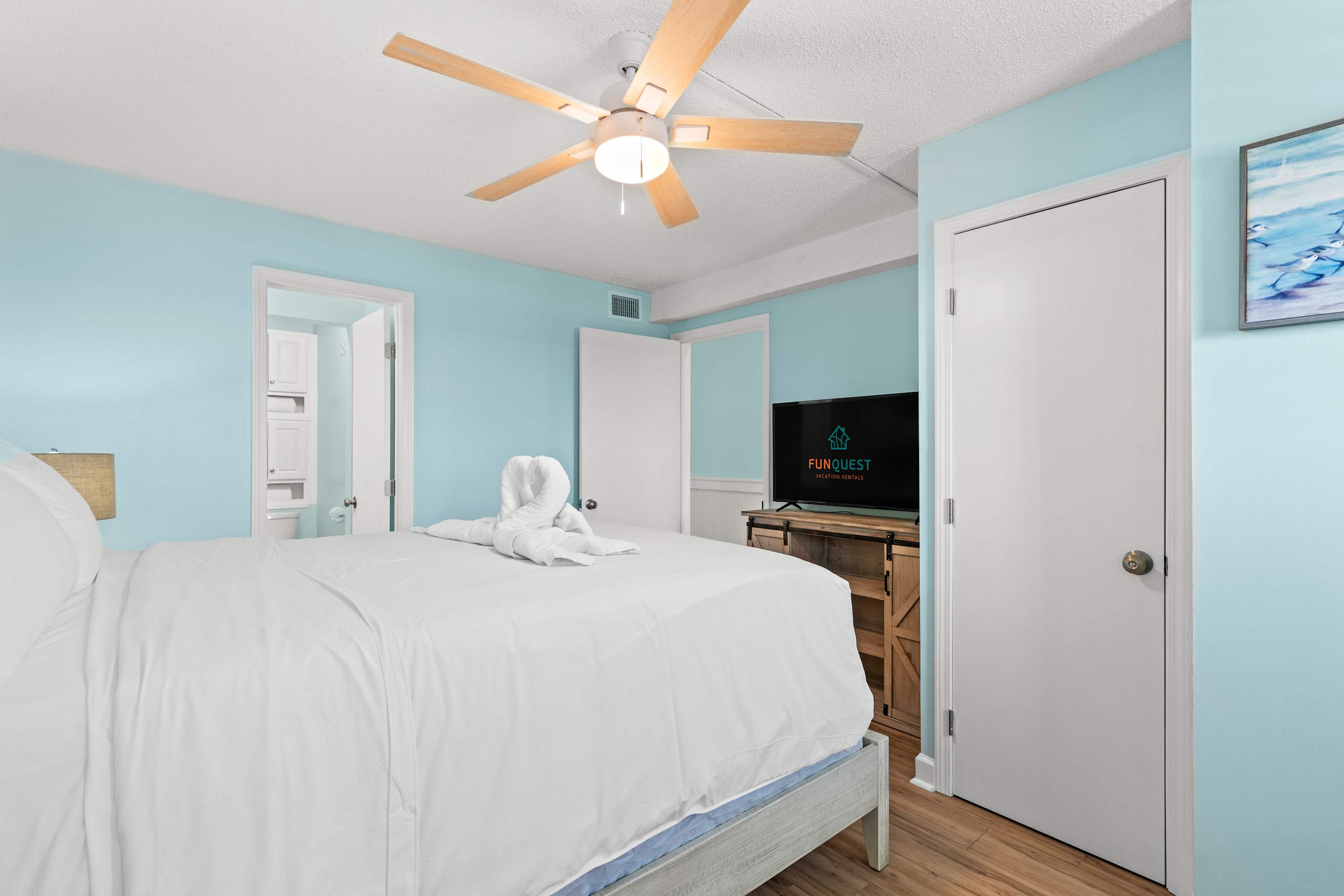 The Summit 1419 – Bedroom with a queen bed, light blue walls, ceiling fan, and flat-screen TV.