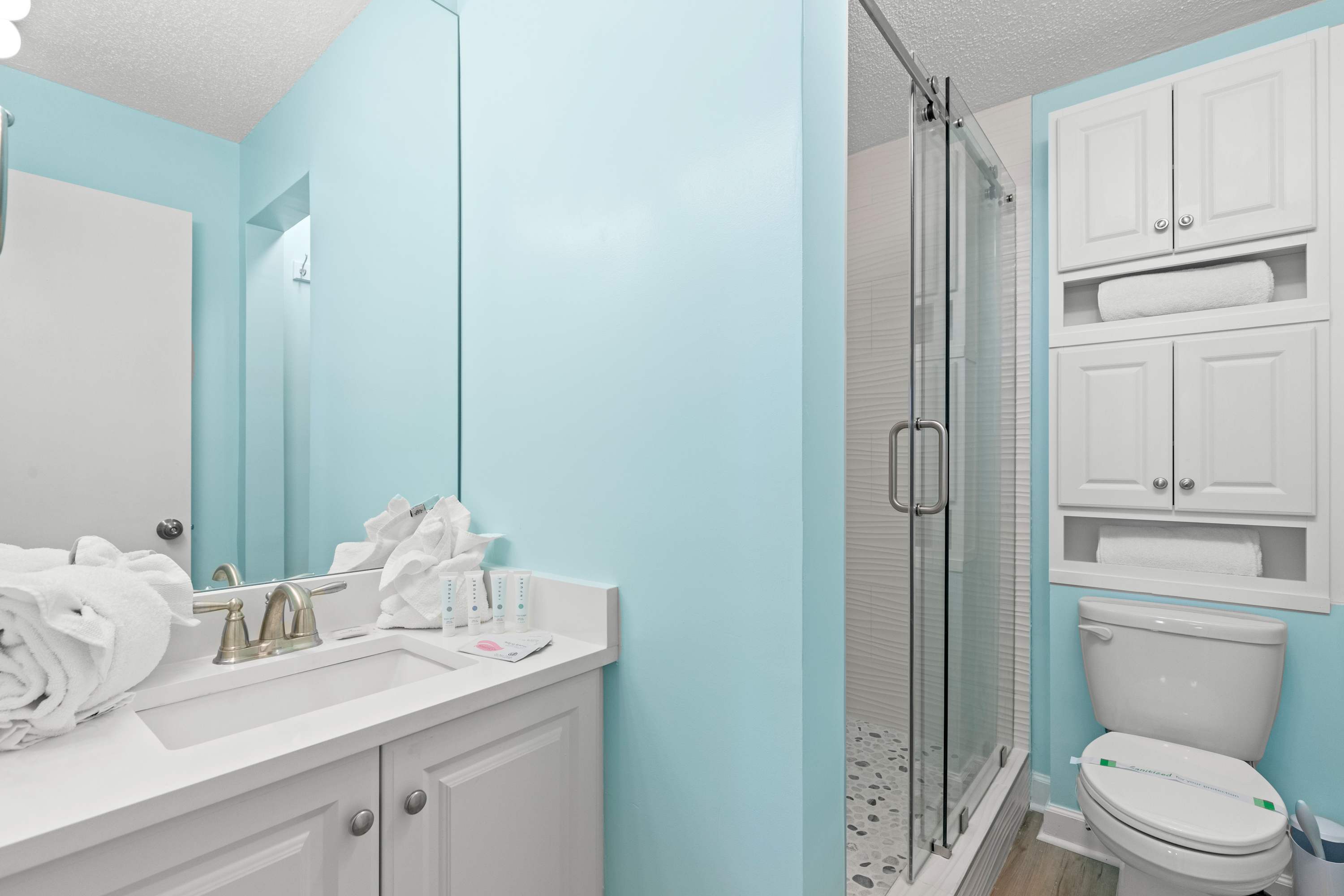 The Summit 1419 – Bathroom with light blue walls, glass shower, white vanity, and towels on the counter.