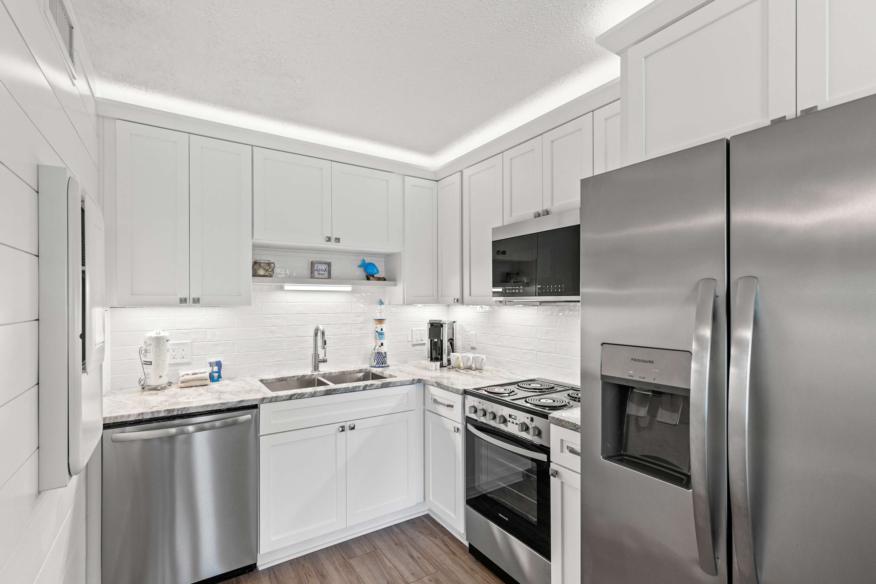 The Summit 1419 – Modern kitchen with stainless steel appliances, white cabinets, marble countertops, and lighted backsplash.