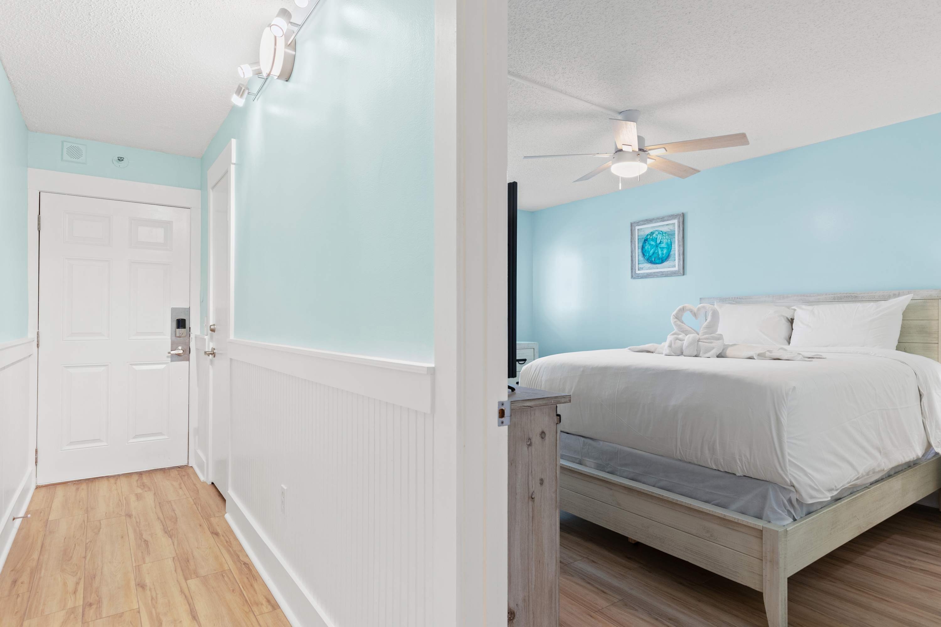 The Summit 1419 – Bright bedroom with a queen bed, wood floor, and turquoise walls, visible from a hallway.