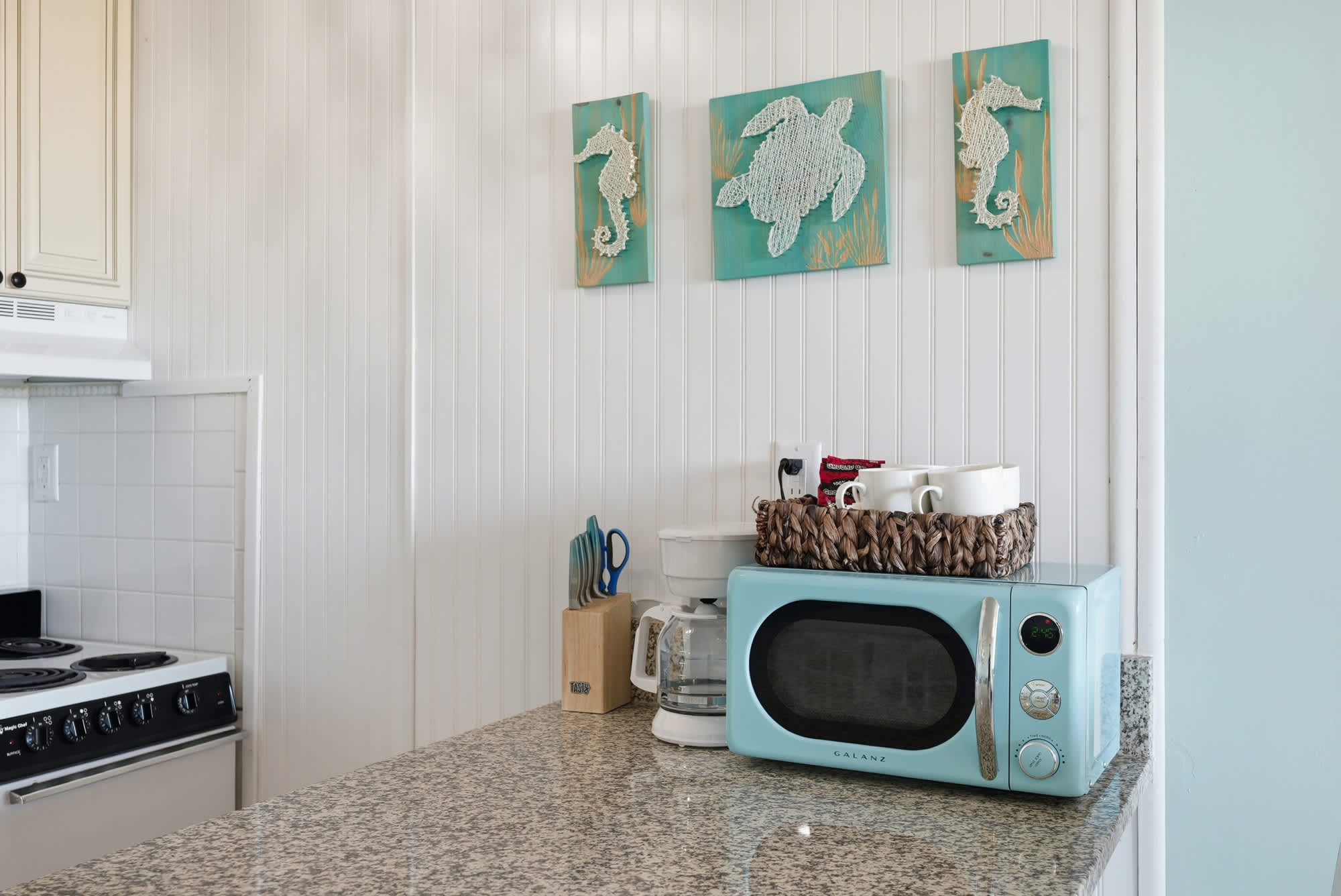 Top Of The Gulf  602 – Compact kitchen with granite countertop, blue microwave, and decorative sea-themed wall art.
