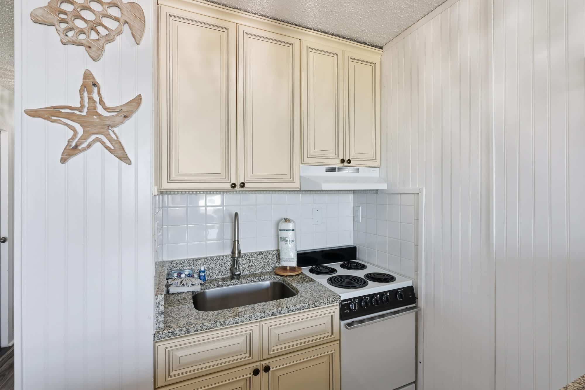 Top Of The Gulf  602 – Compact kitchen with granite countertop, stove, sink, and decorative ocean-themed wooden accents.