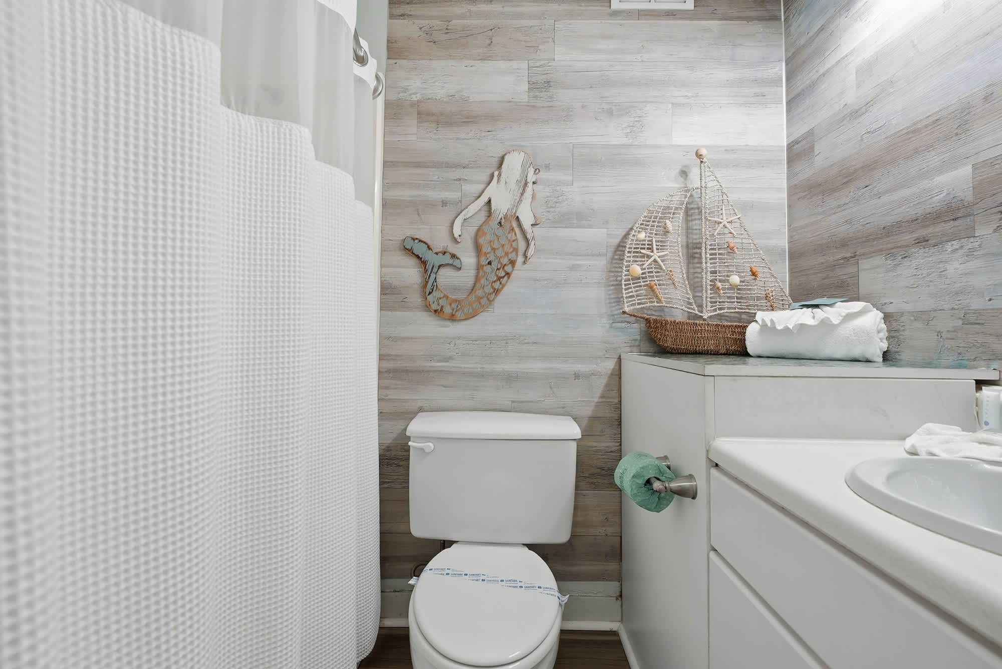 Top Of The Gulf  602 – Small bathroom with a toilet, sink, and nautical decor elements.
