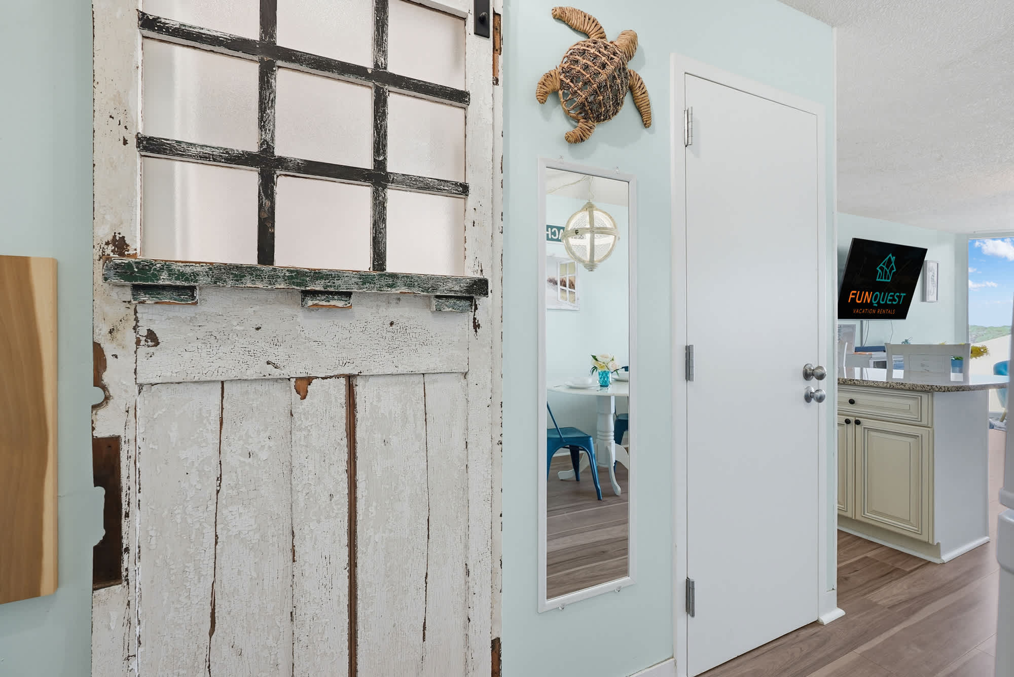 Top Of The Gulf  602 – Interior view of a vacation rental with a rustic door, mirror, and kitchenette in light colors.
