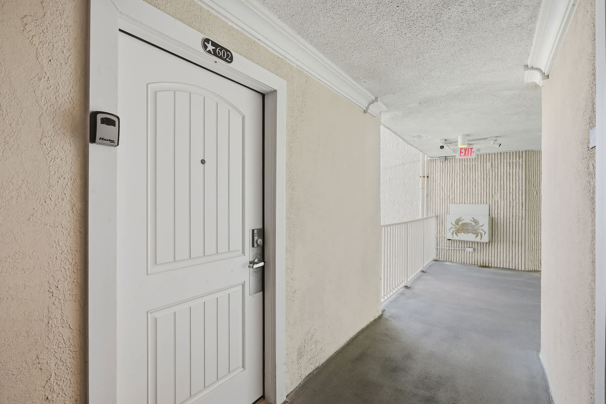 Top Of The Gulf  602 – White door with room number 602 in a corridor, featuring light-colored walls and a crab artwork.