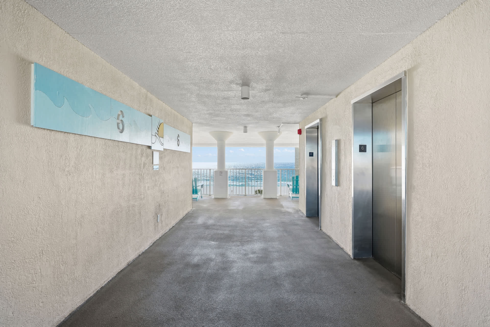 Top Of The Gulf  602 – Building corridor with elevators and view of the ocean through the railing.