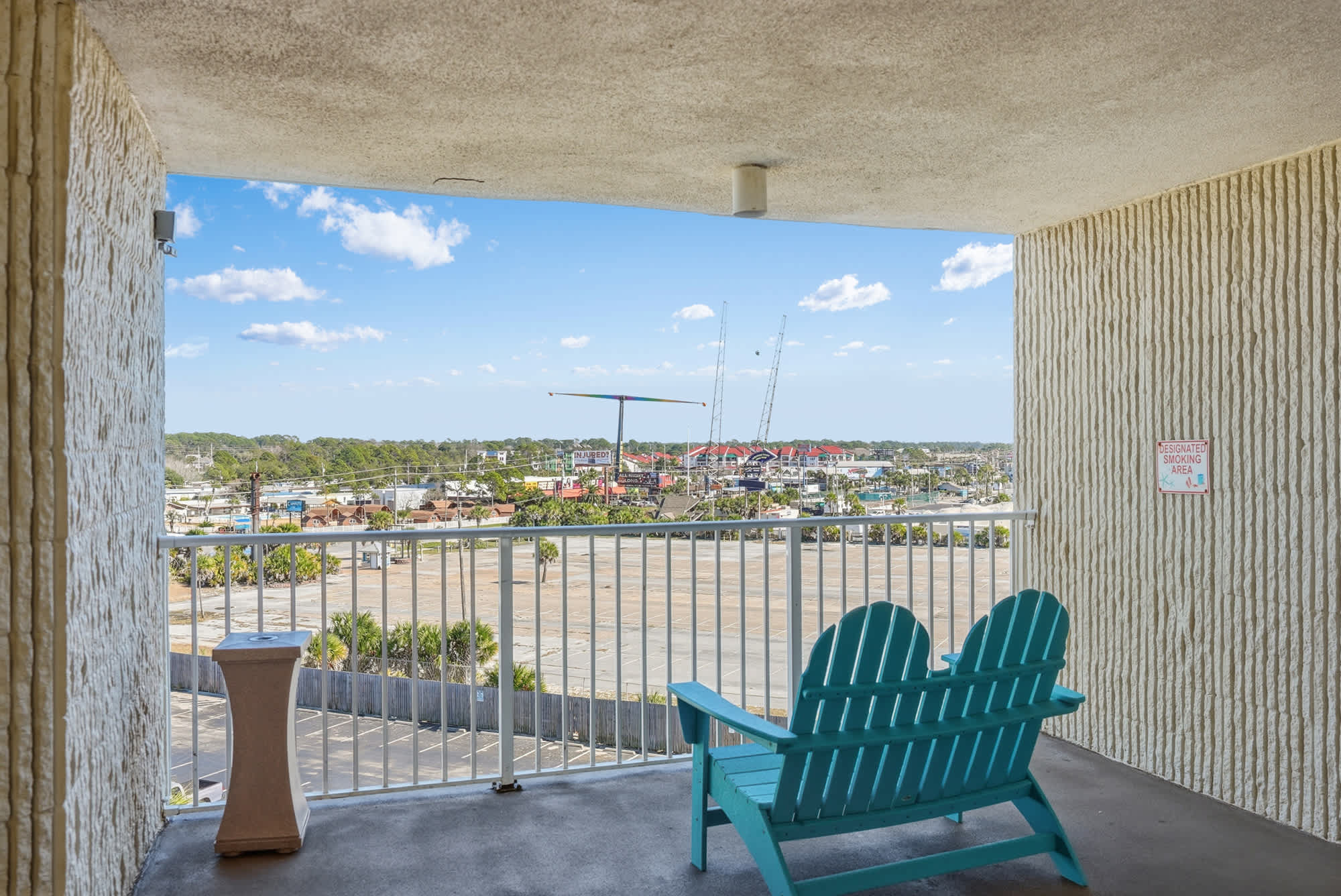 Top Of The Gulf  602 – Balcony view with turquoise chairs overlooking a parking lot and nearby buildings.