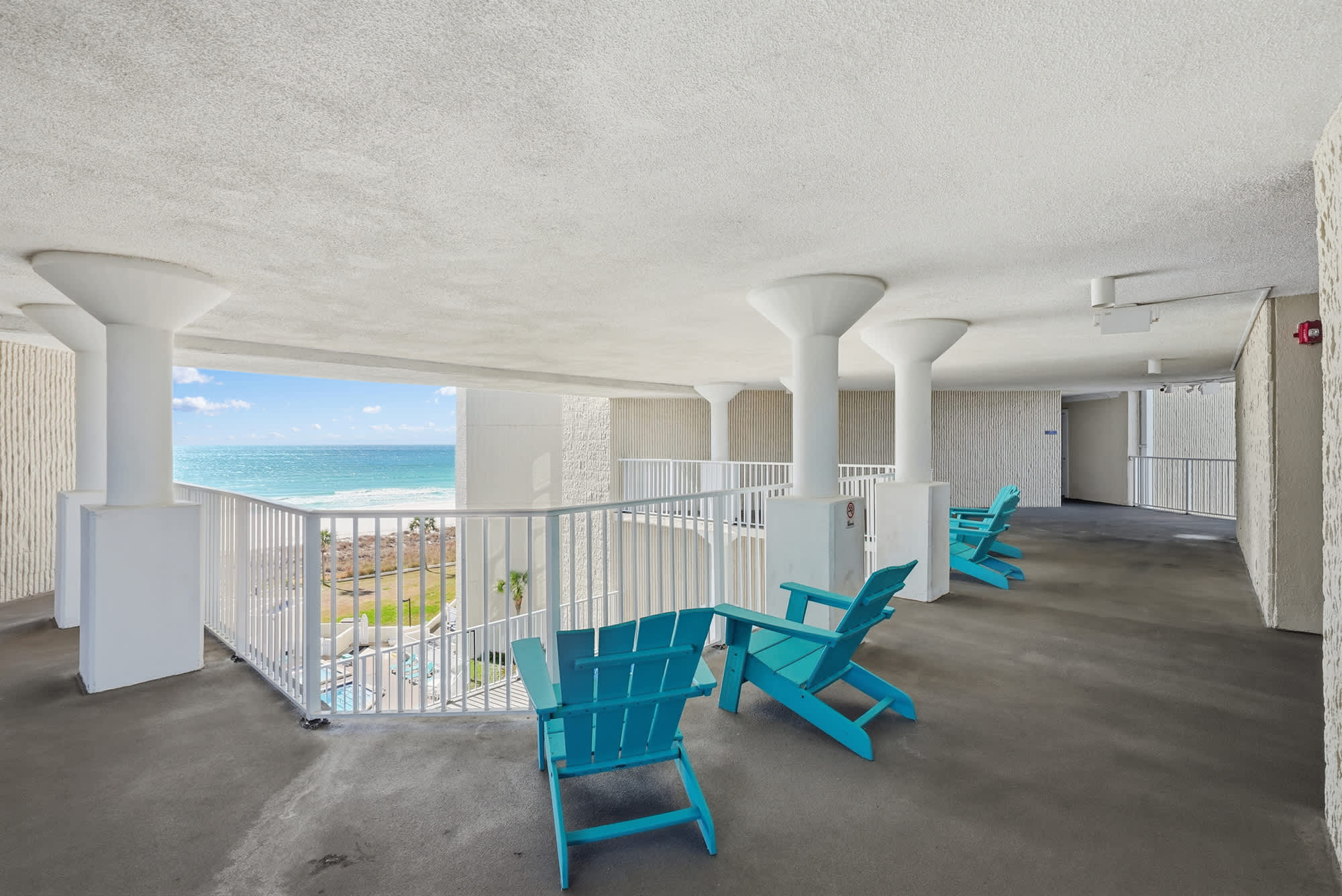 Top Of The Gulf  602 – Balcony view with turquoise chairs overlooking the ocean and pool area.