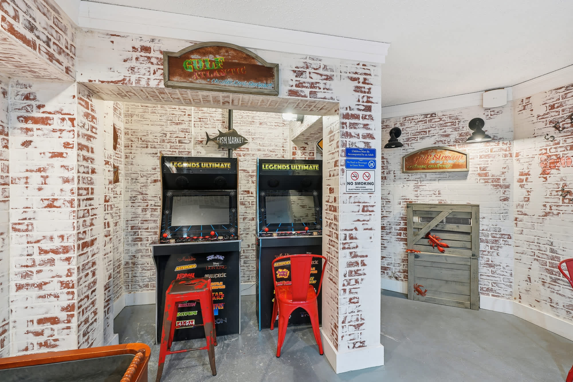 Top Of The Gulf  602 – Game room with arcade machines, red stools, and a rustic brick wall design.