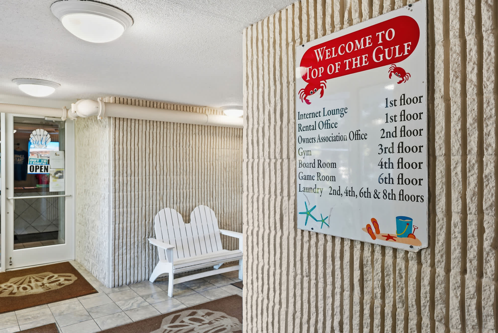Top Of The Gulf  602 – Entry area with a sign listing amenities, decorative seating, and tile flooring.