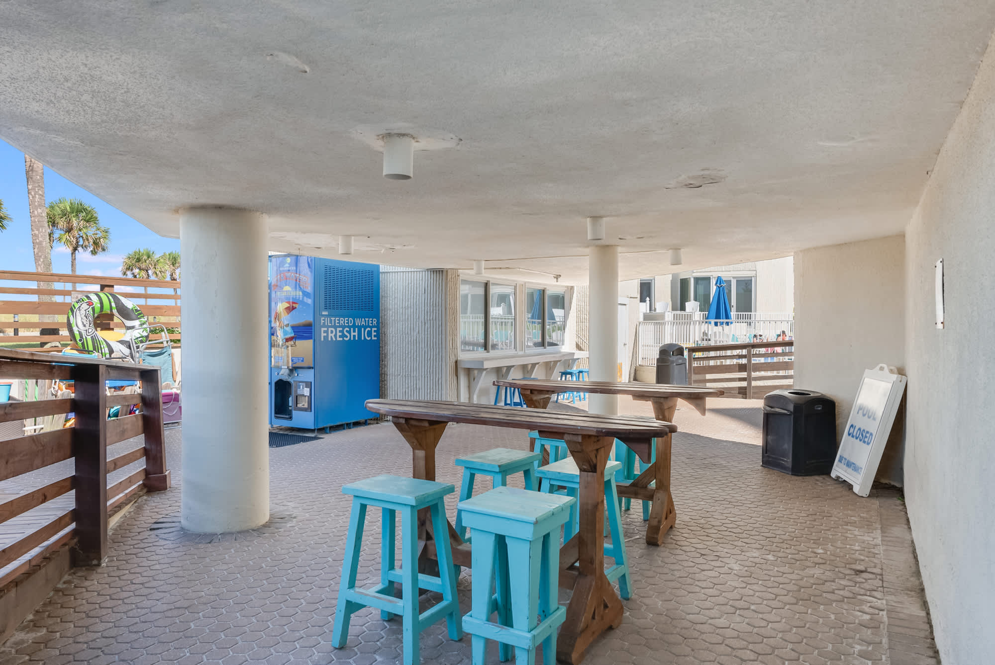 Top Of The Gulf 306 – Outdoor seating area with turquoise stools, filtered water station, and view of palm trees.