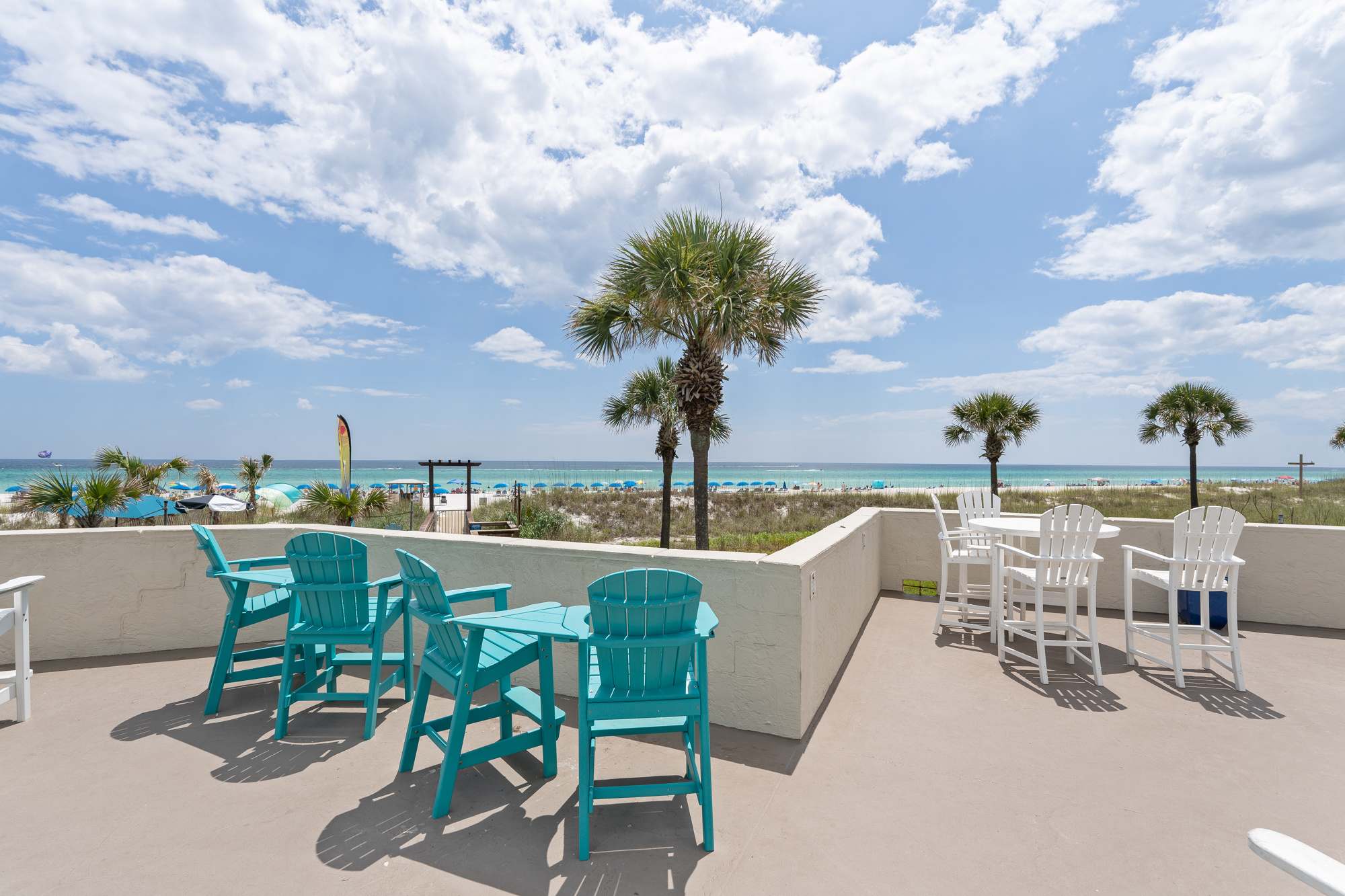 Top Of The Gulf 704 – View of beach with turquoise chairs and palm trees from a balcony at Top Of The Gulf 704.