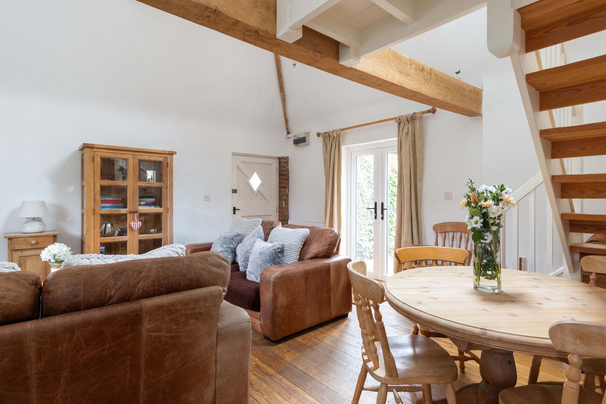 The open-plan living space combines kitchen, dining and seating areas beneath exposed beams, creating a sociable and cosy environment.