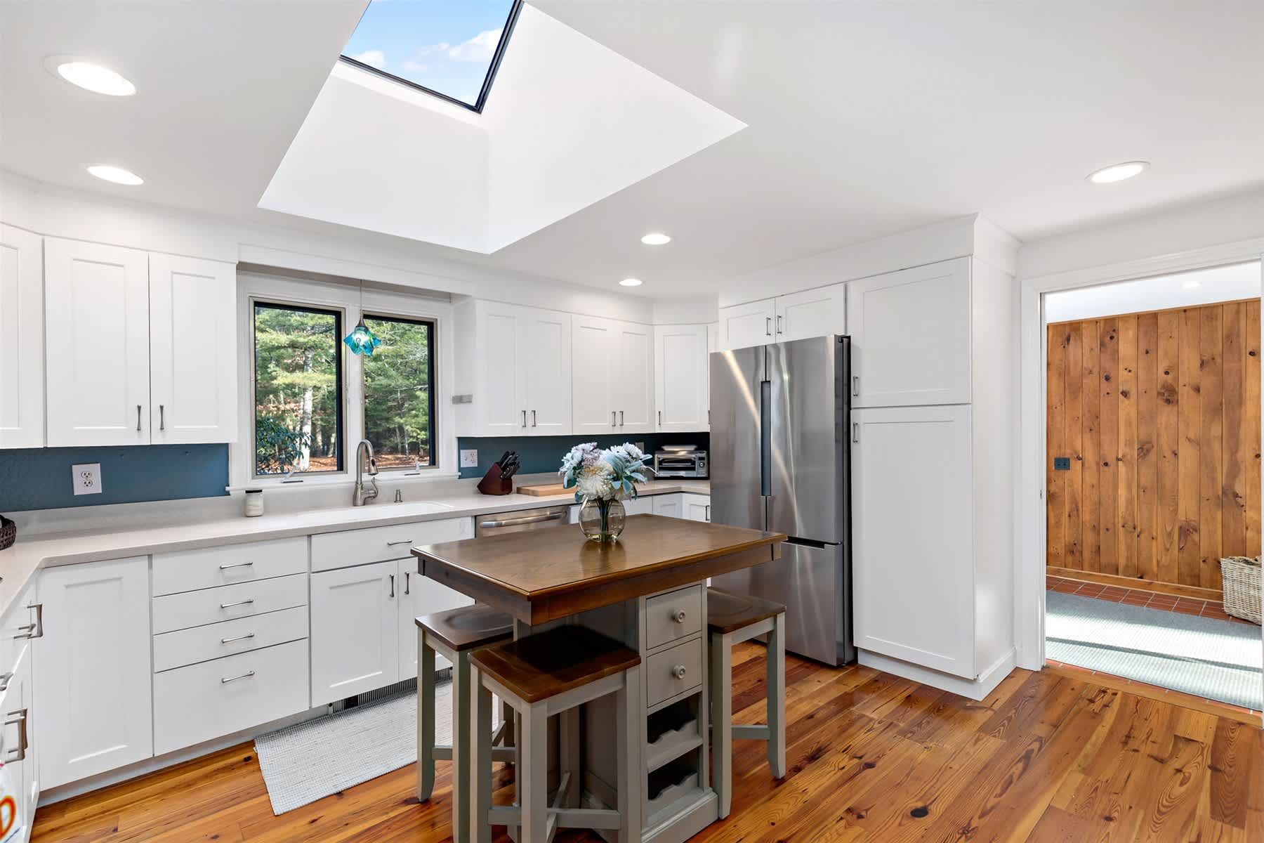 Bright Cape Cod kitchen with generous cabinets, double door refrigerator, and prep island. Easy flow to living and dining spaces.