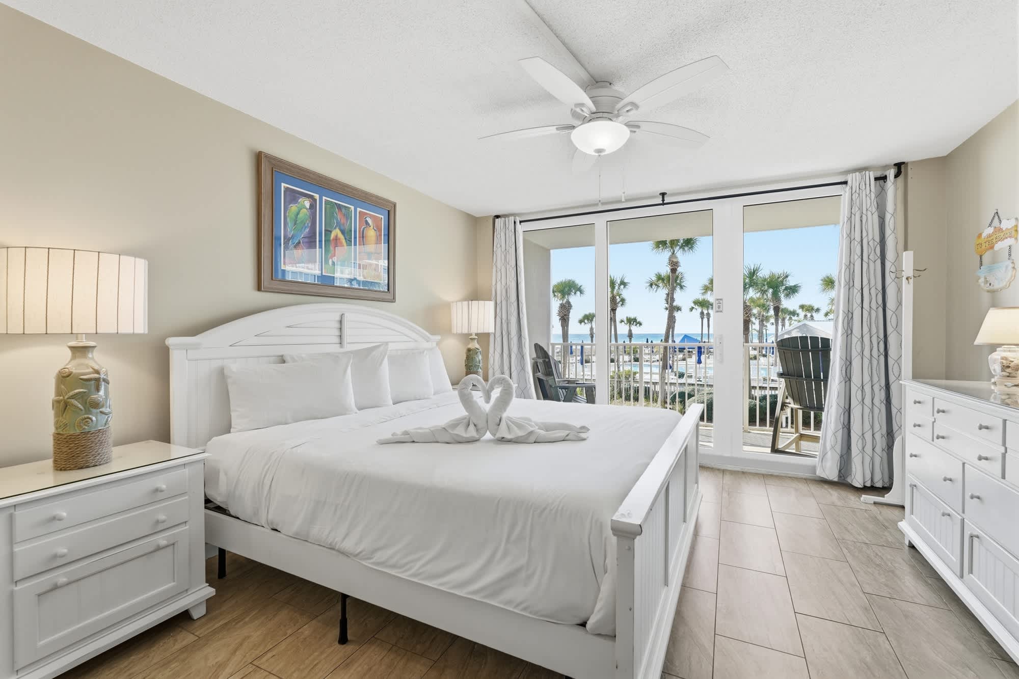 Dunes C104 – Bright bedroom with a king bed, dresser, and balcony offering views of palms and ocean.