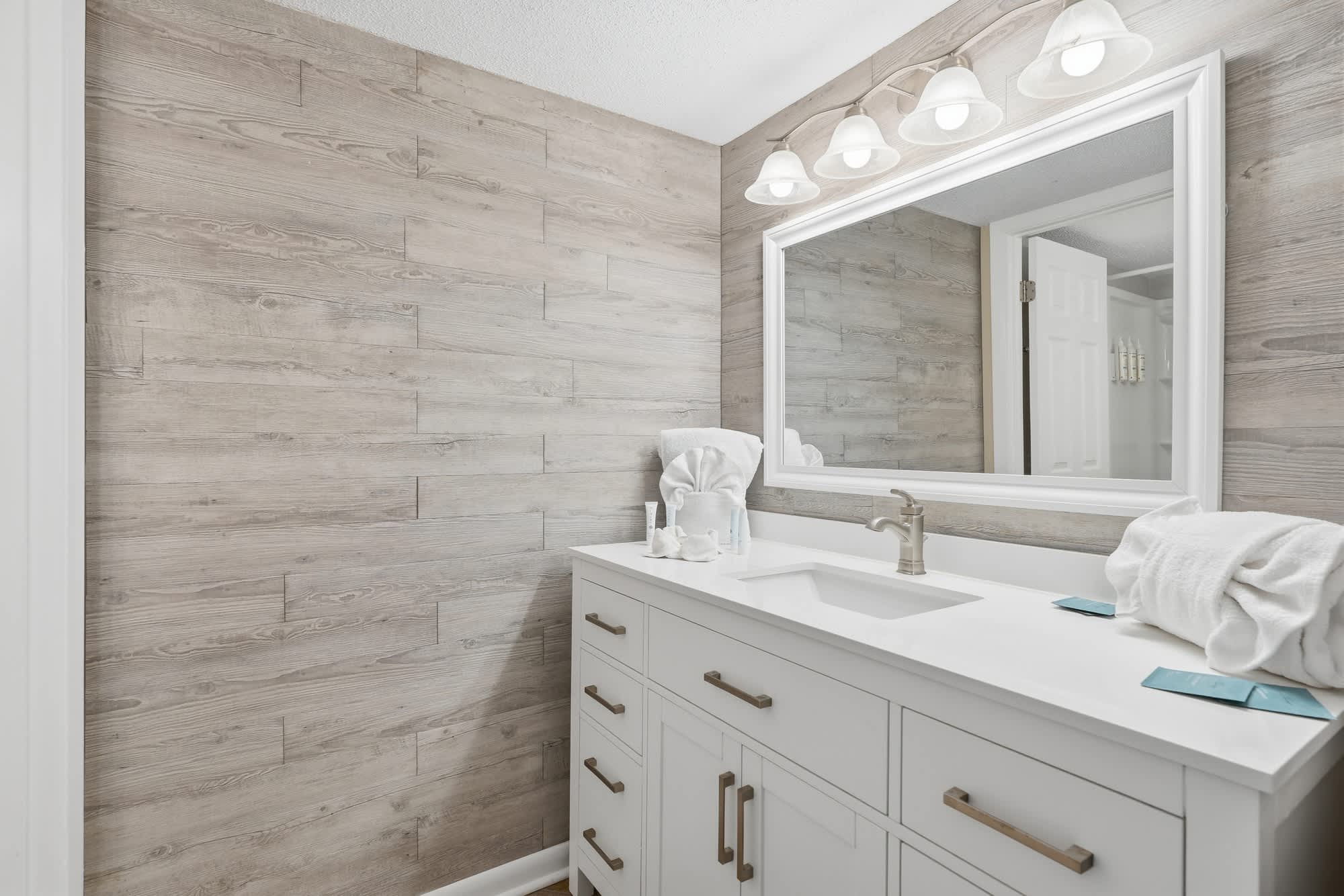 Dunes C104 – Modern bathroom with a double sink, large mirror, light wood wall, and white cabinetry.