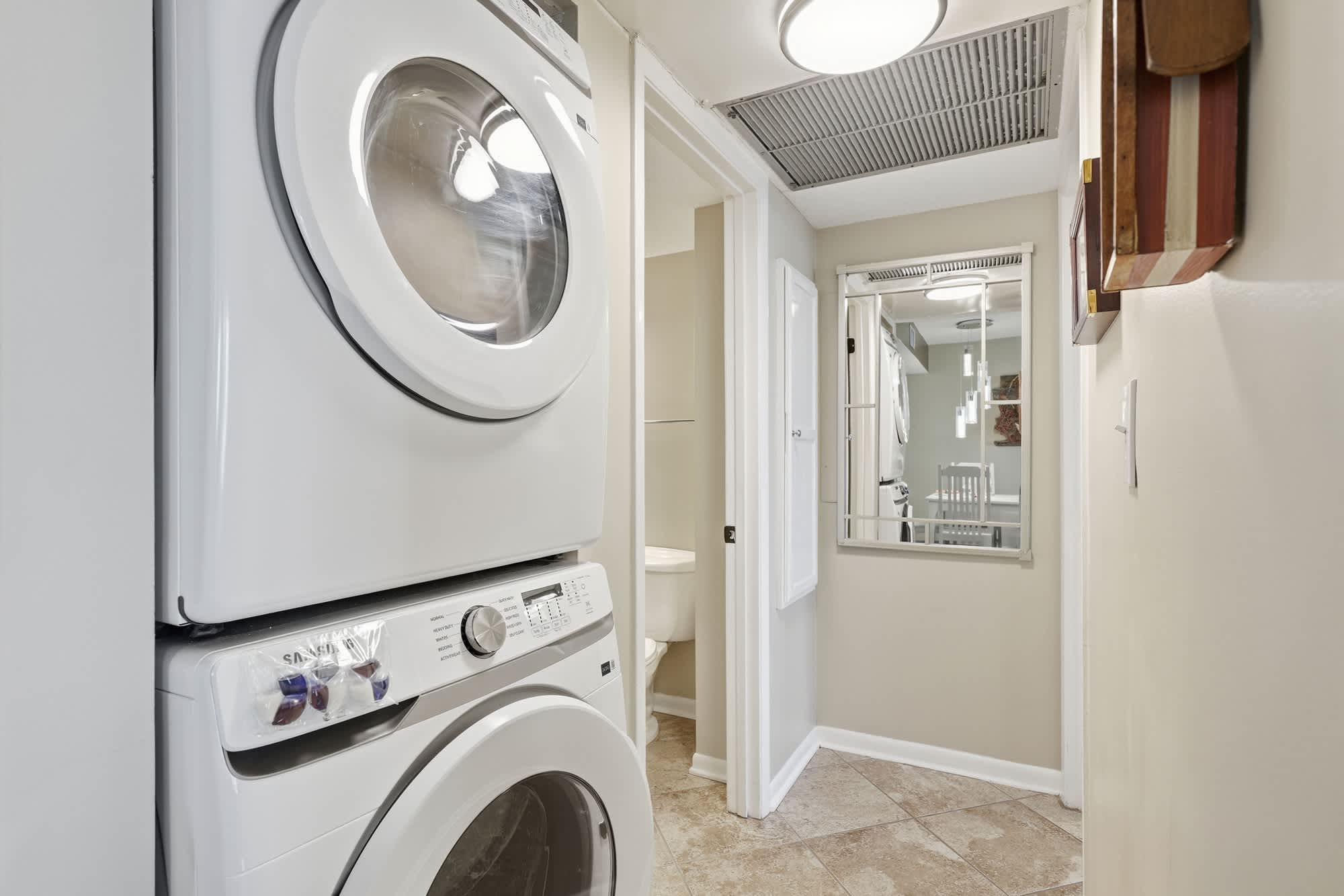 Dunes C104 – Laundry area with stacked washer and dryer, hallway leading to bathroom and living space.