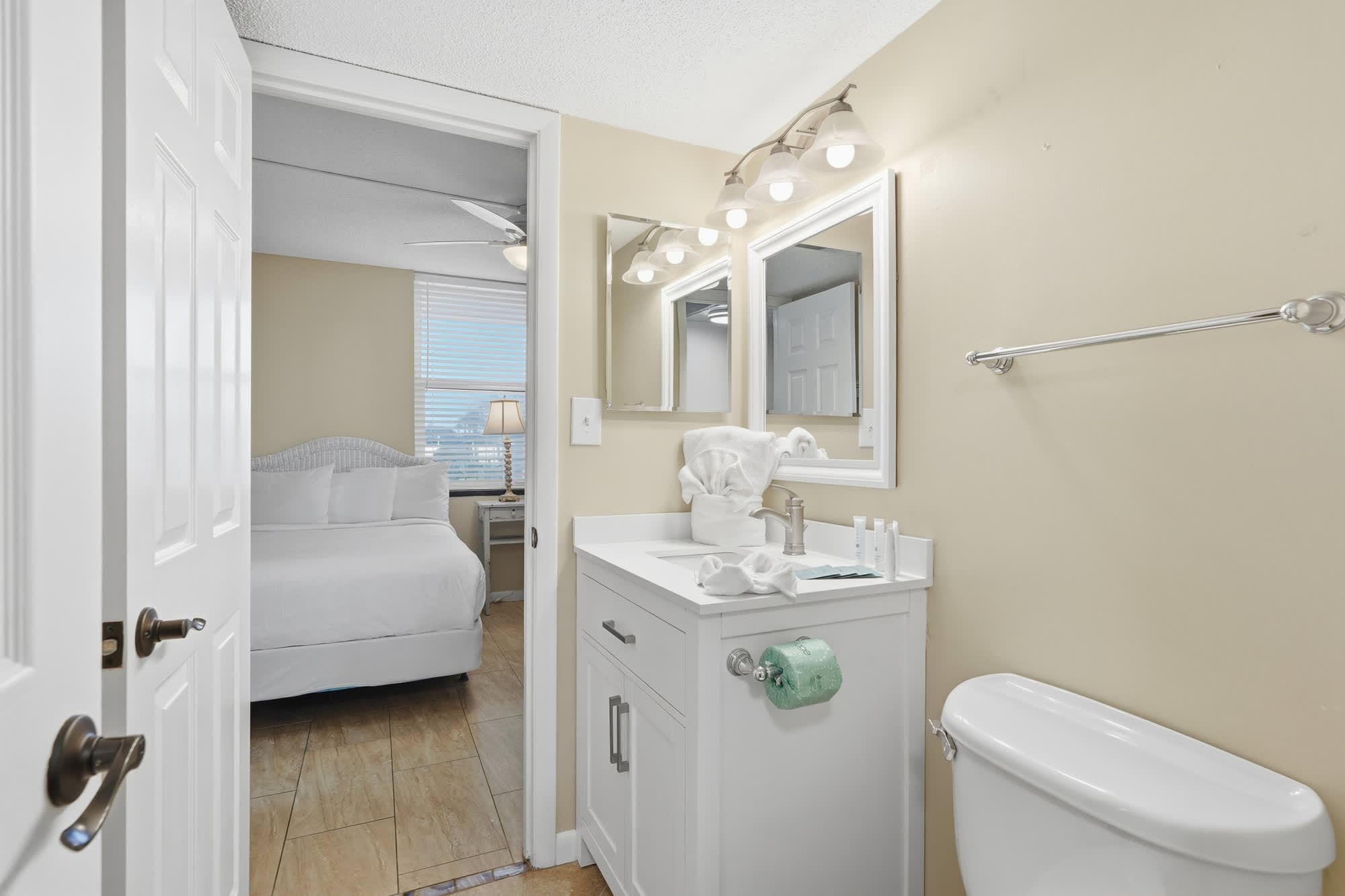 Dunes C104 – Bathroom with white vanity, mirror, and view into a bedroom with a bed and window.