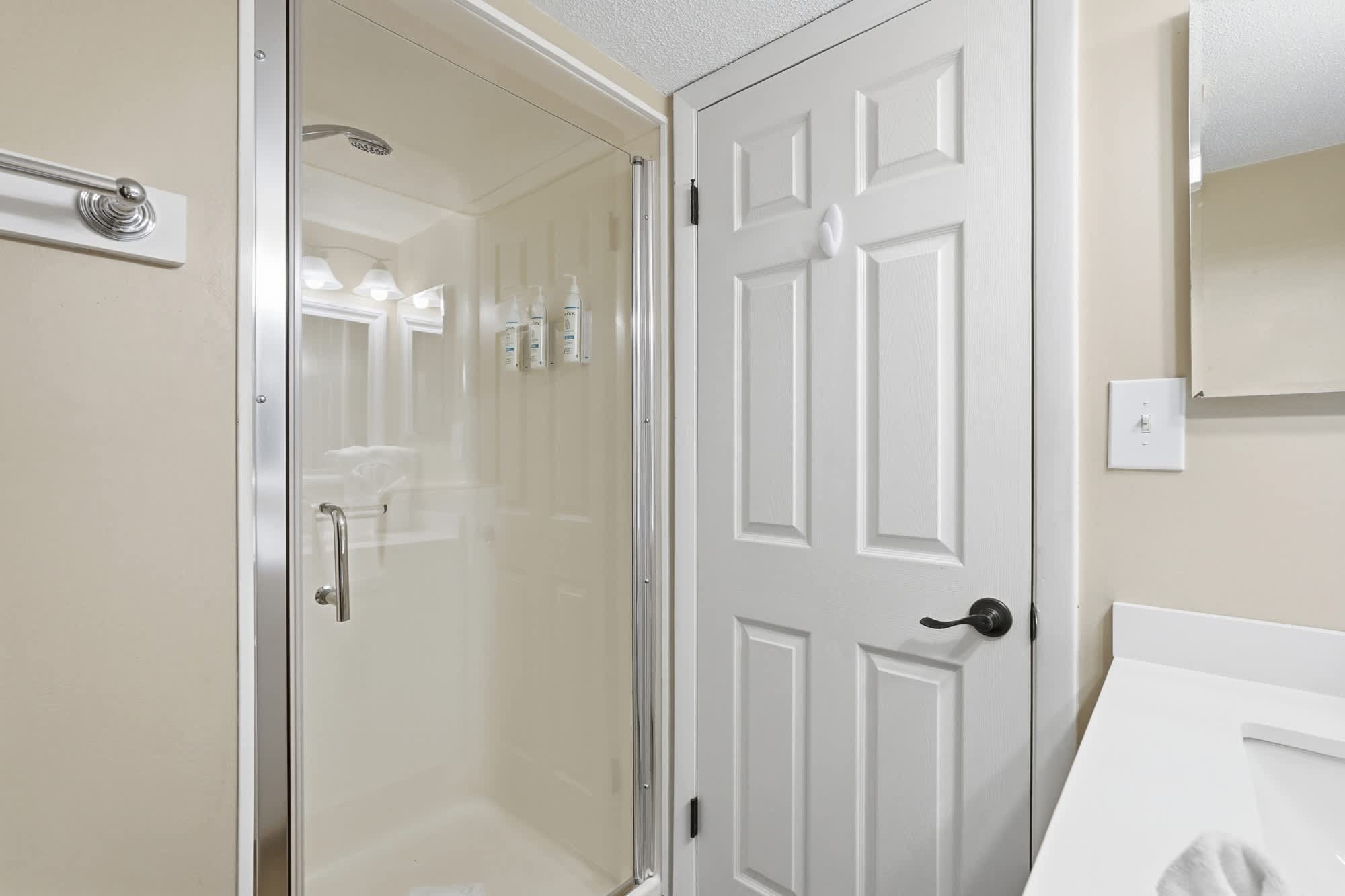 Dunes C104 – Bathroom with shower, mirror, and door, featuring neutral colors and toiletries on the wall.