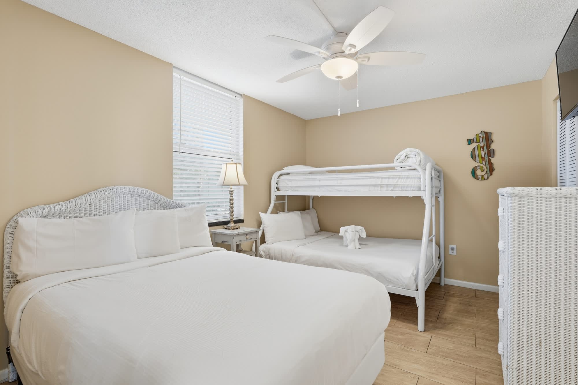 Dunes C104 – Bedroom with a queen bed, bunk bed, lamp, and dresser against beige walls.