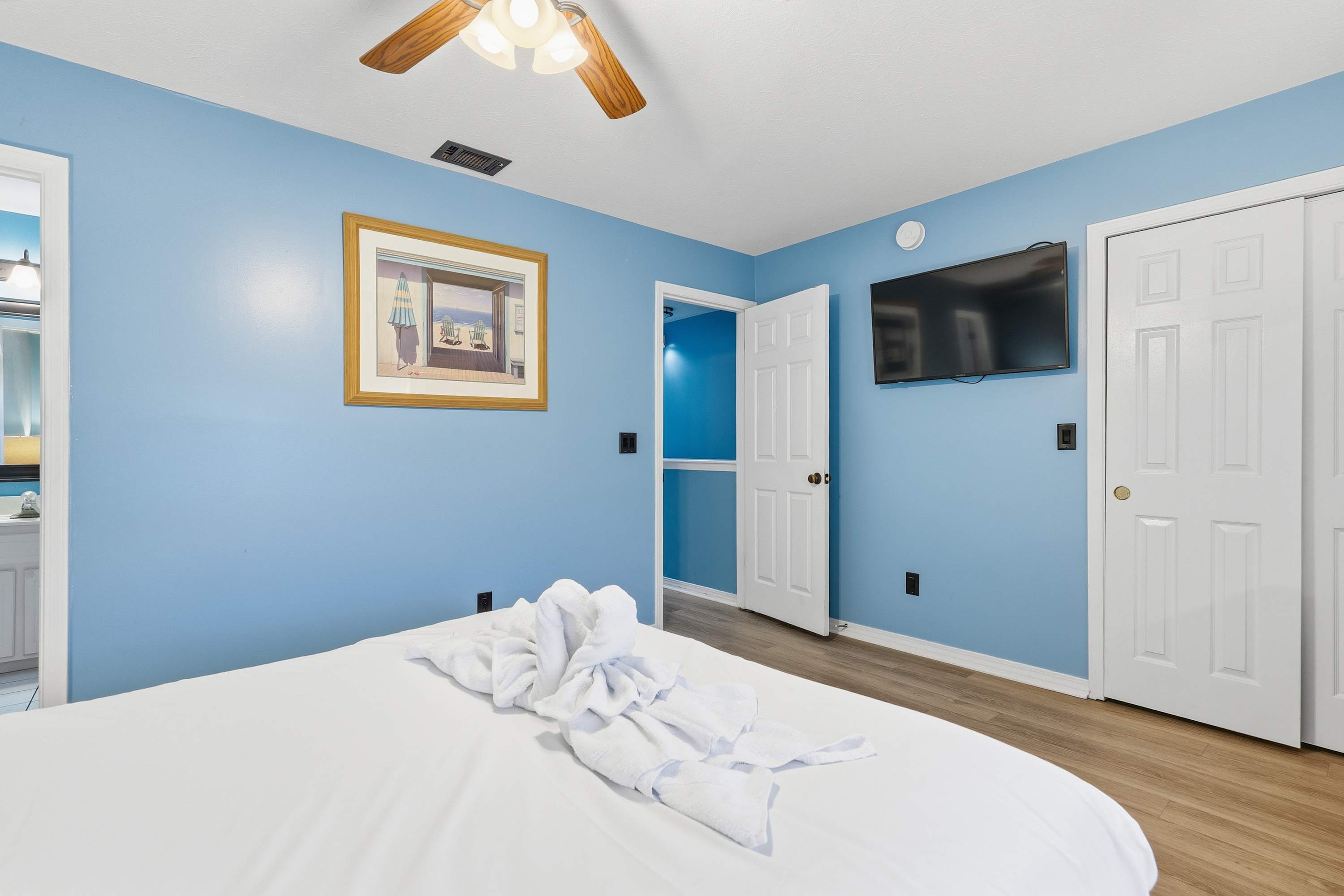 135 Grande Island Blvd – Bedroom with blue walls, a TV, framed artwork, and a towel sculpture on the bed.