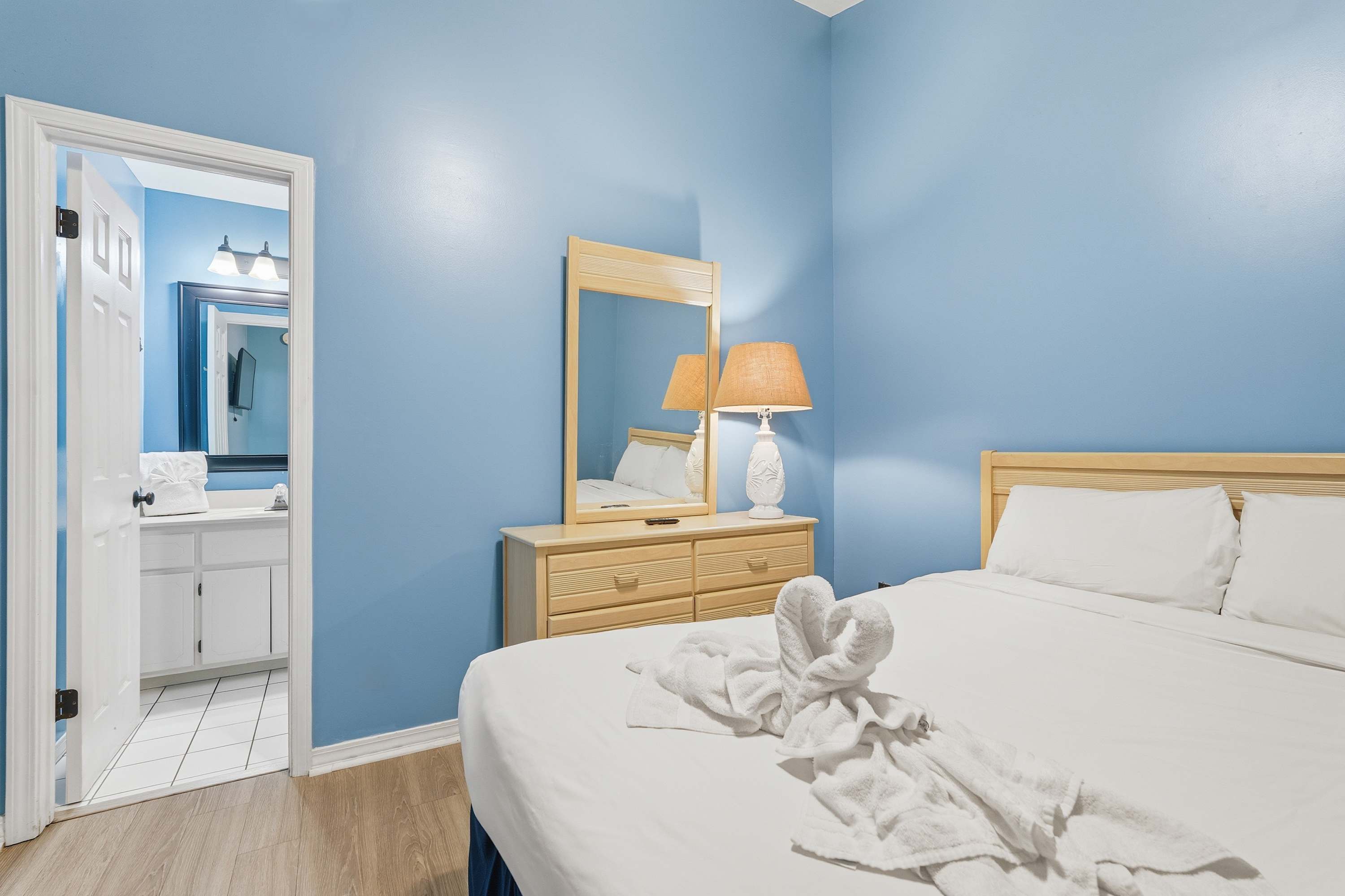 135 Grande Island Blvd – Cozy bedroom with blue walls, dresser, lamp, and adjoining bathroom visible through open door.