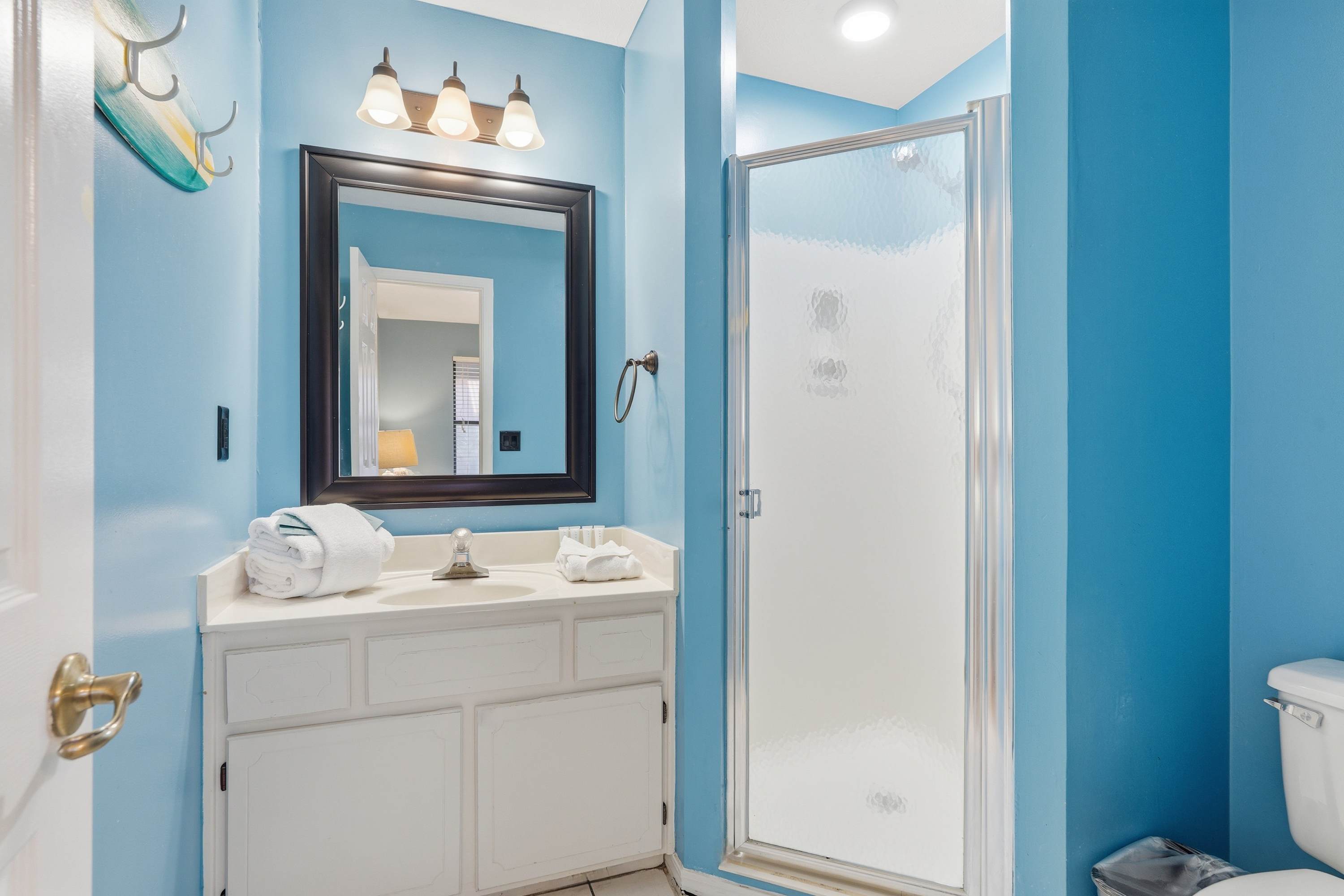 135 Grande Island Blvd – Bright blue bathroom with a shower, vanity, mirror, and white towels.