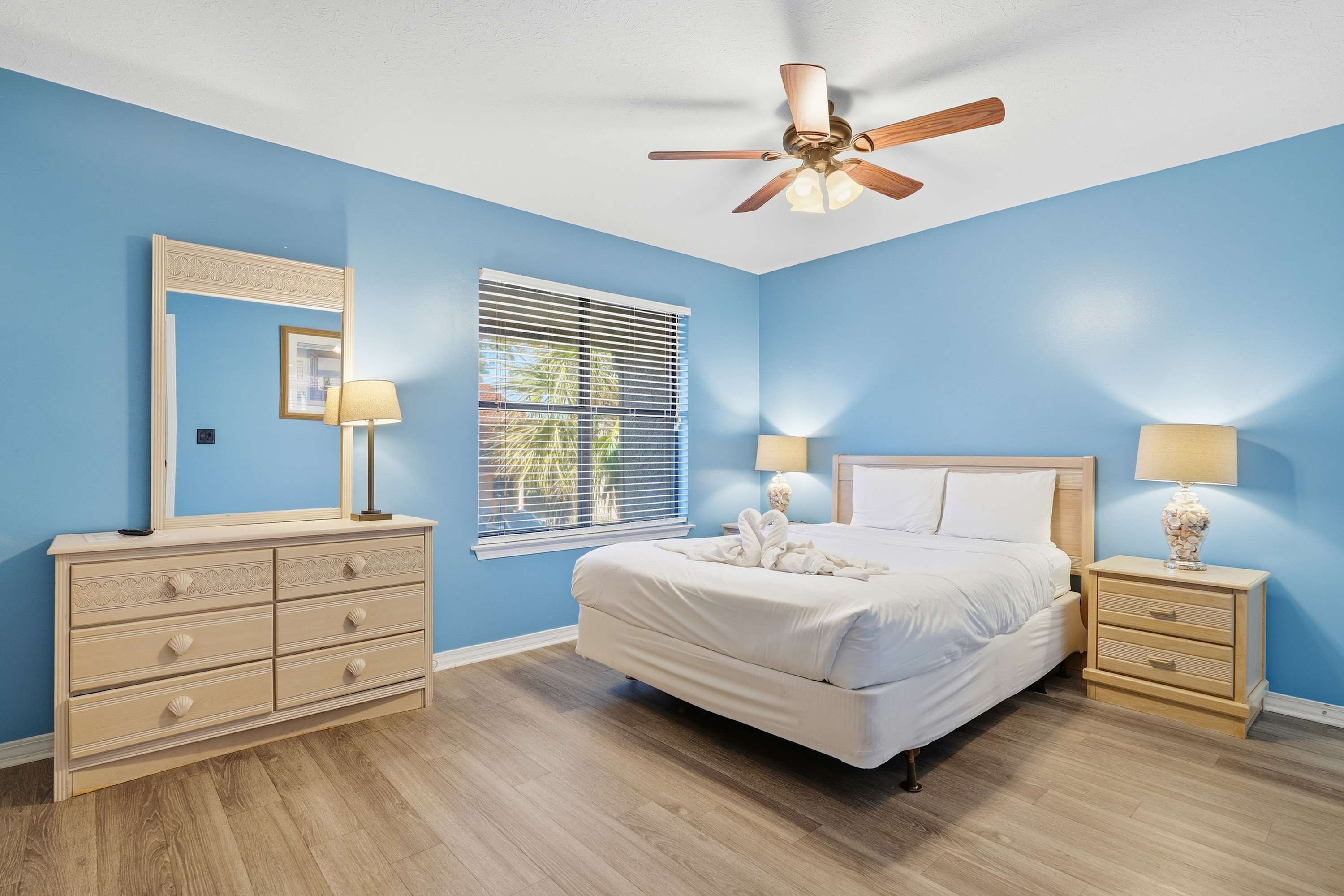 135 Grande Island Blvd – Bedroom with blue walls, queen bed, dresser, nightstands, lamps, and window showing palm trees outside.