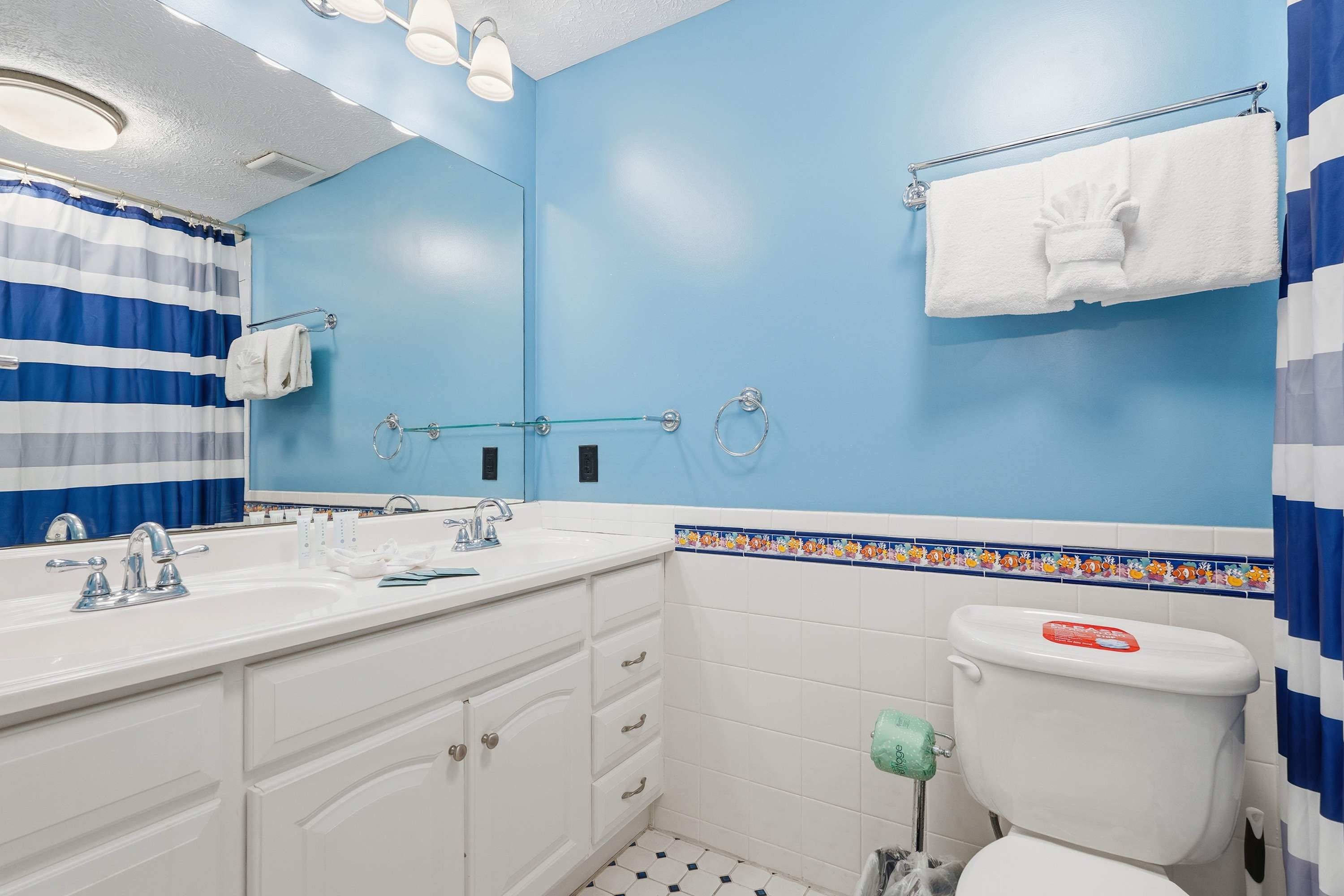 135 Grande Island Blvd – Blue-themed bathroom with double sinks, striped shower curtain, and decorative tile border.