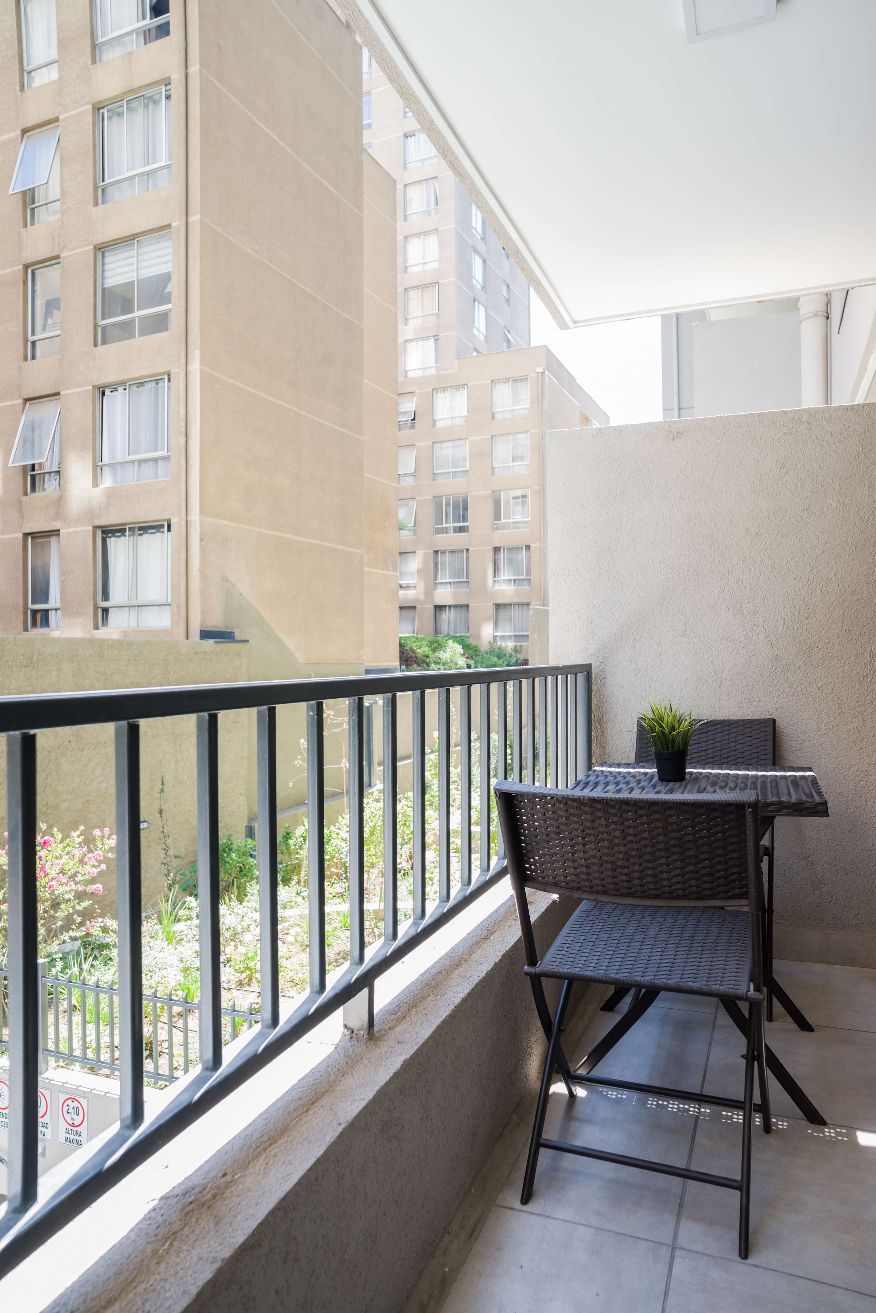 Enjoy morning coffee on the private balcony, with two woven chairs, a potted plant, and views over the landscaped courtyard.