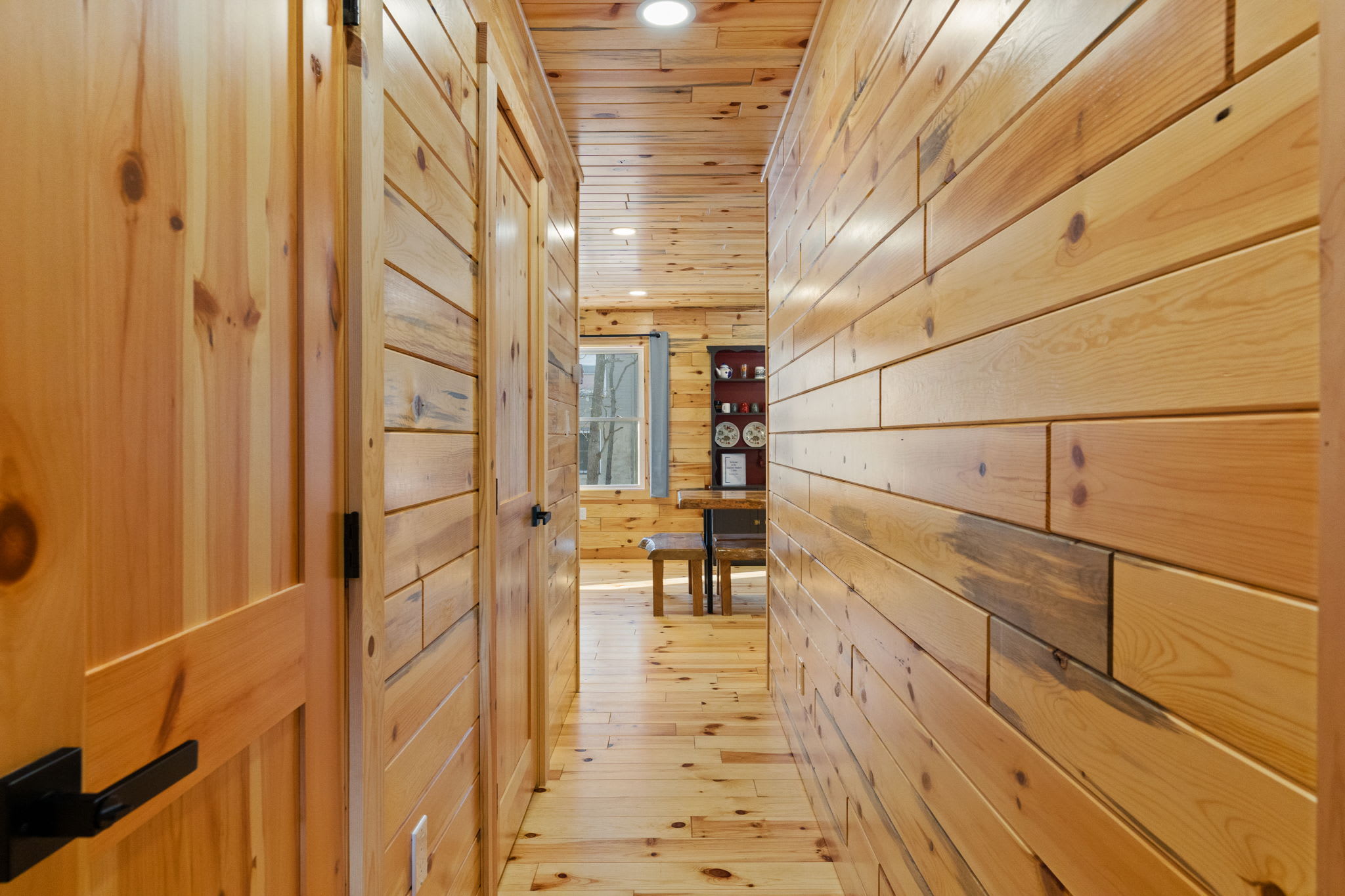 A warm hallway of natural log walls leads to cozy bedrooms throughout the cabin
