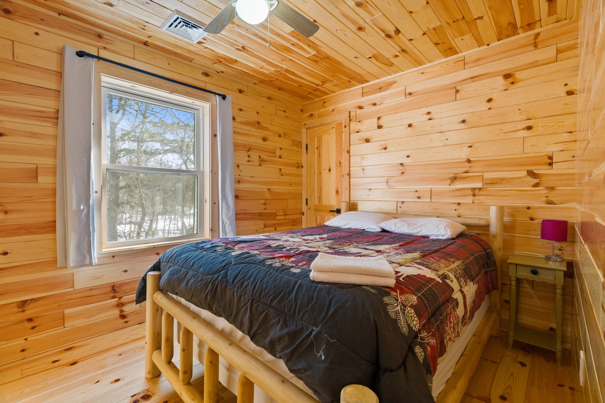 A quiet lower-level bedroom with plush bedding and a window onto the woods