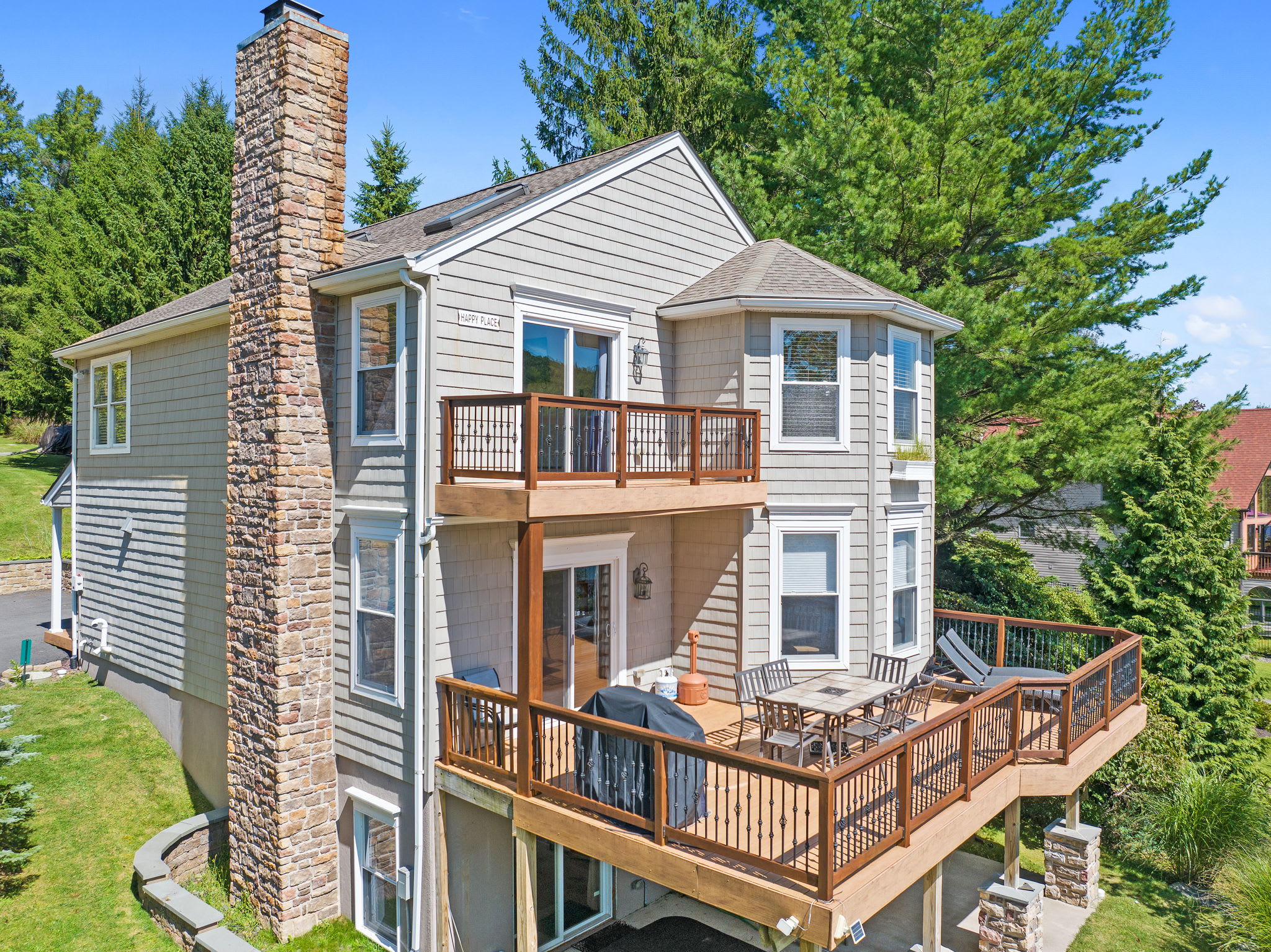 Multi-level lake house with deck, hot tub, and balcony surrounded by trees