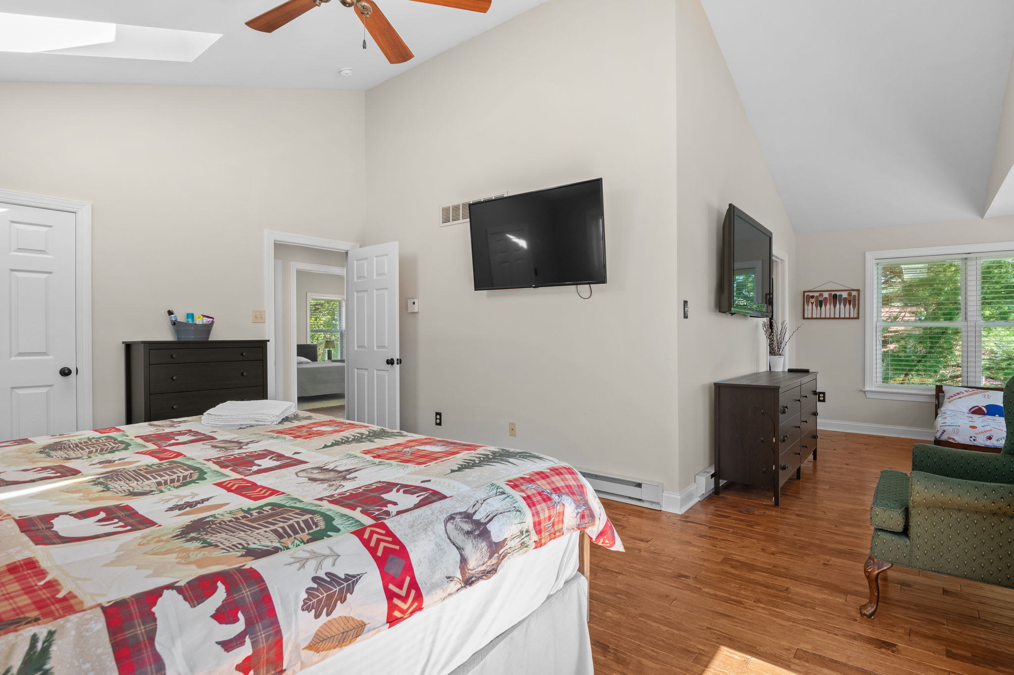 Relax in this bright bedroom with a TV, ceiling fan, and views of the trees