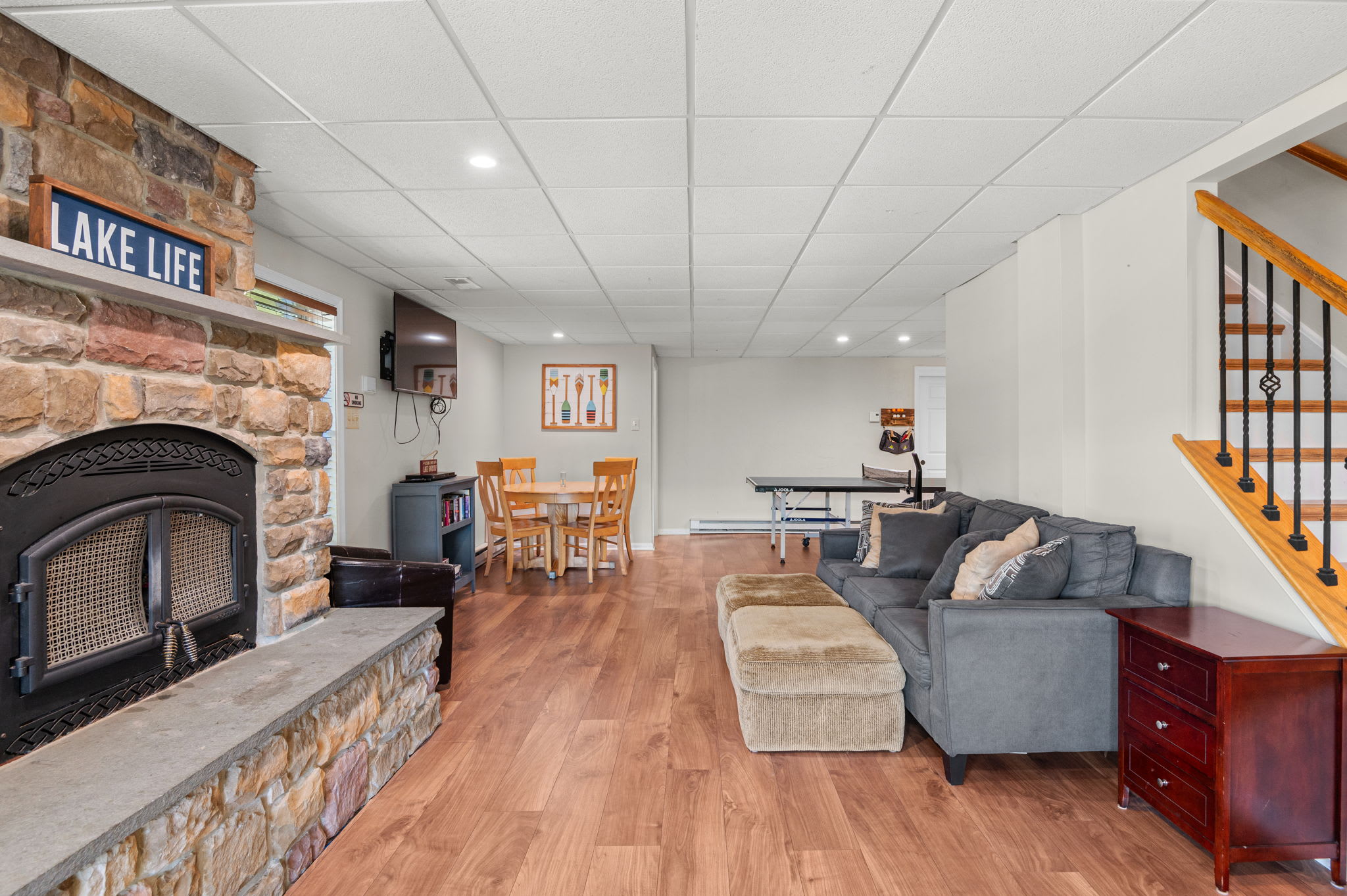 Lower-level rec room with a stone fireplace, cozy seating, and lake house charm